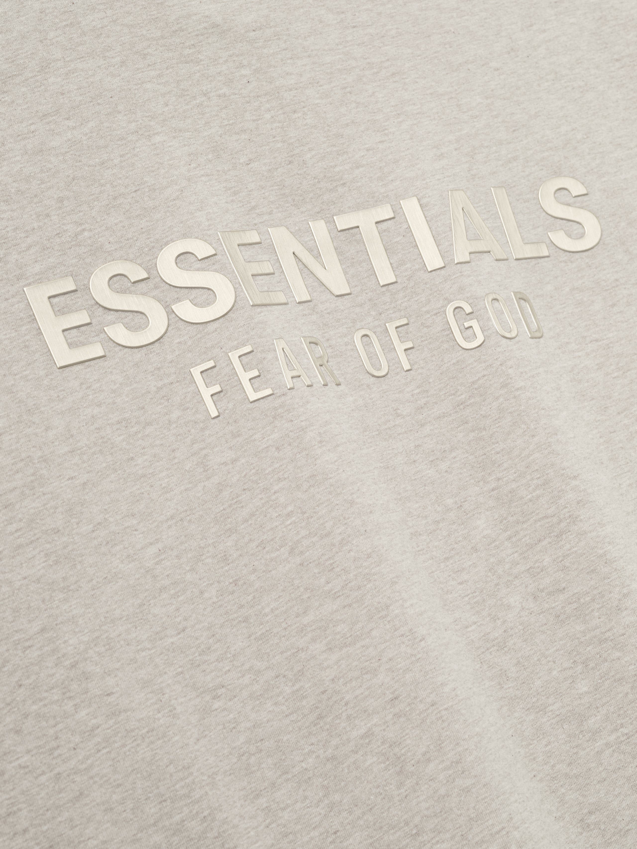 close-up of light beige cotton jersey tee with embossed ESSENTIALS Fear of God logo on chest area