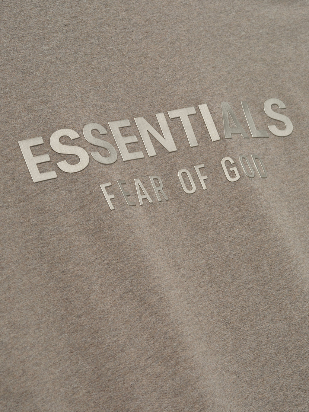 close-up of beige cotton jersey fabric with reflective ESSENTIALS Fear of God logo printed on front chest