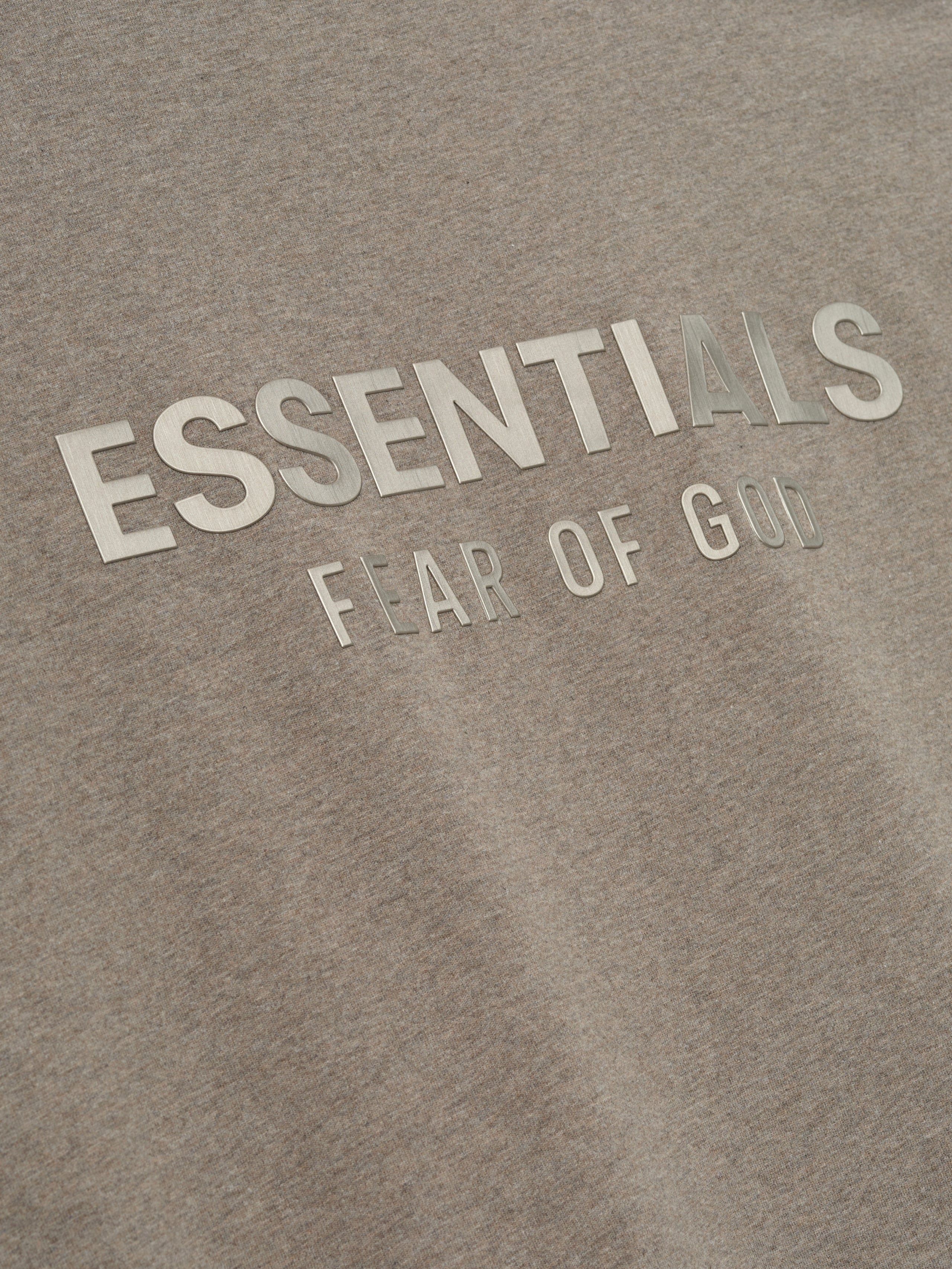 close-up of beige cotton jersey fabric with reflective ESSENTIALS Fear of God logo printed on front chest