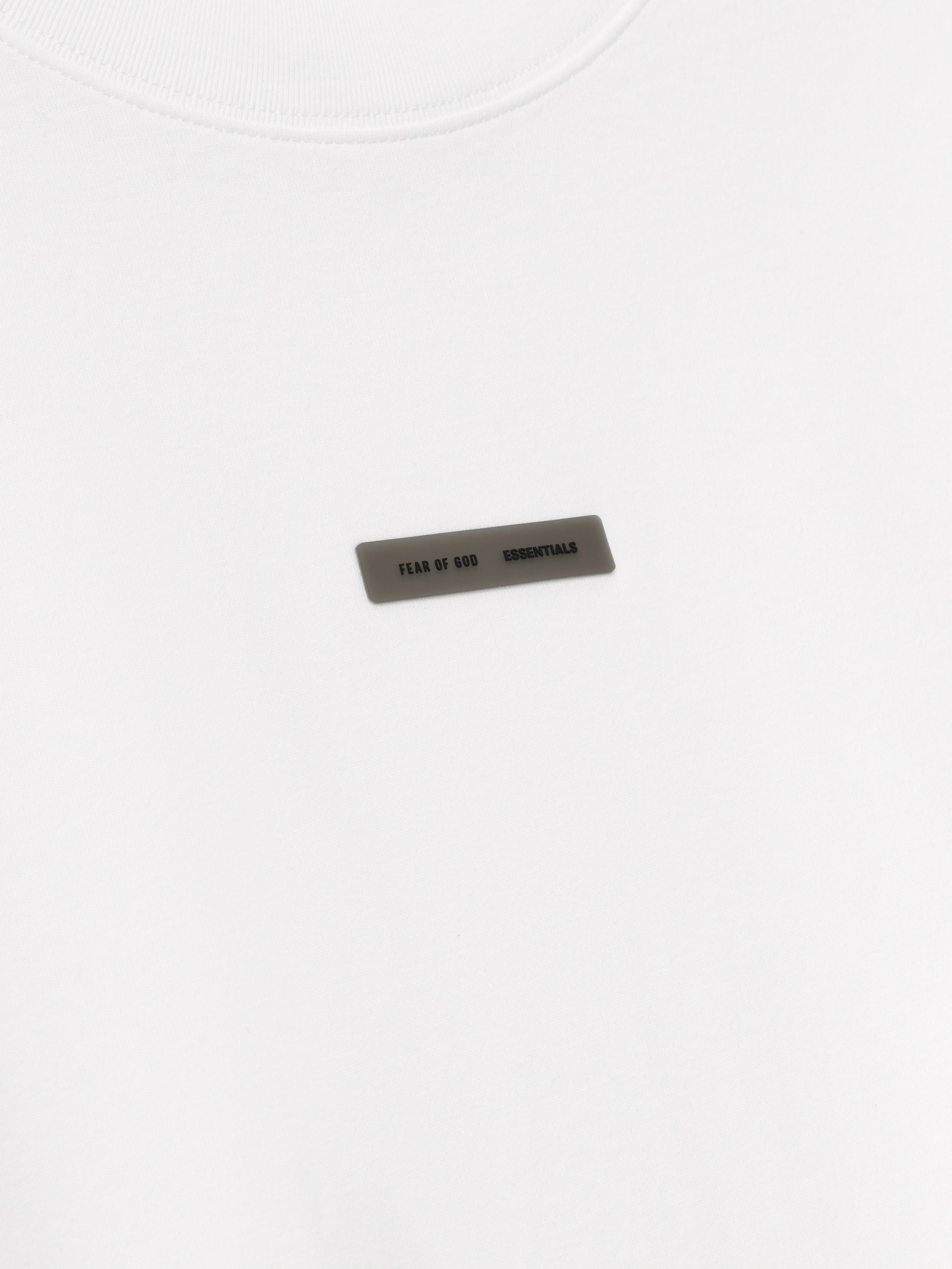 close-up of white lightweight cotton jersey tee with small rectangular Fear of God ESSENTIALS logo patch on chest