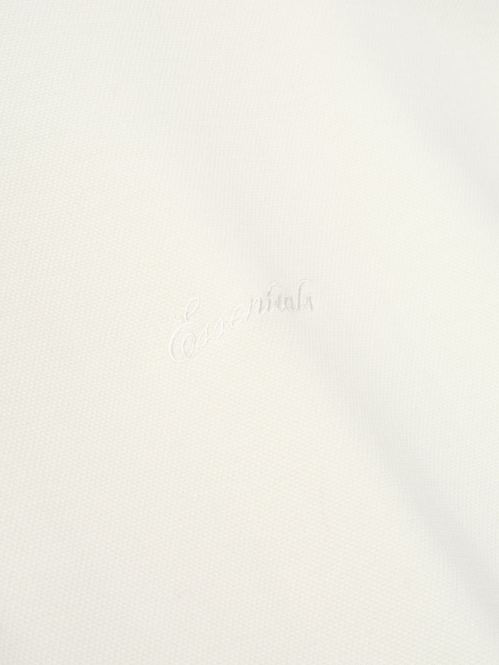 close-up of white medium-weight cotton poly pique fabric with subtle embossed Essentials signature branding