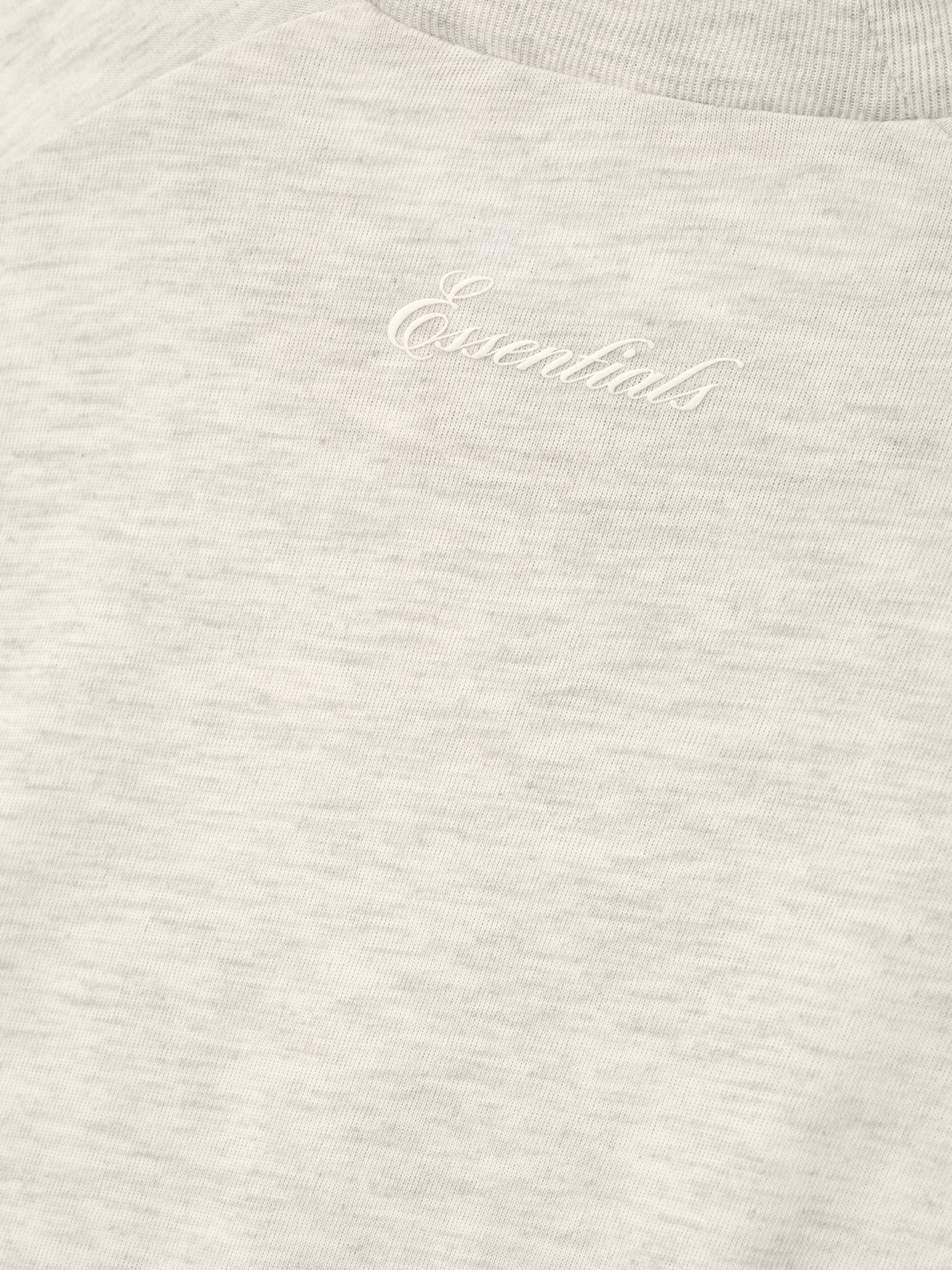 close-up of soft heather natural cotton blend jersey with subtle puff-printed Essentials script logo on women's long sleeve tee