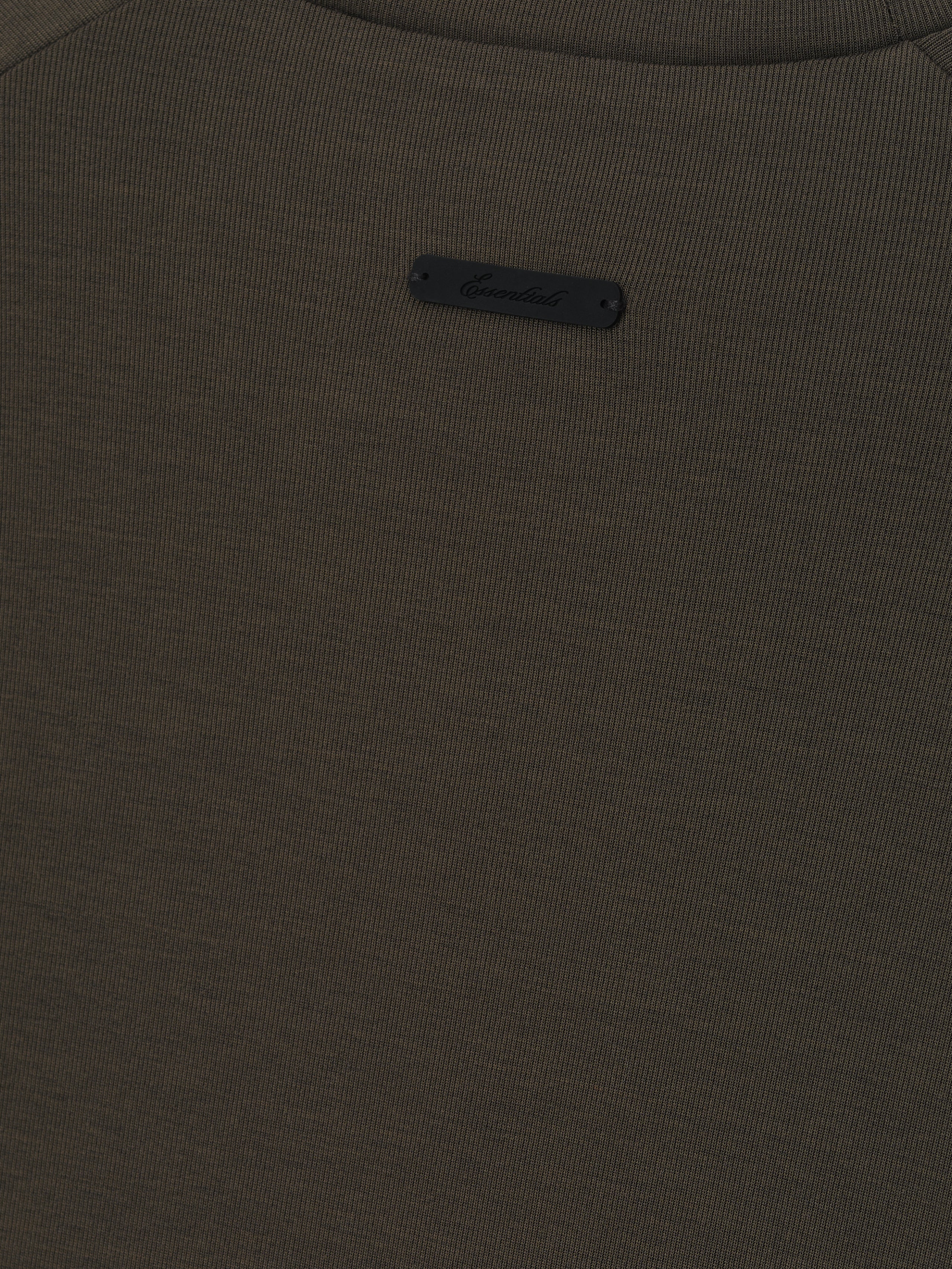 close-up of dark olive ribbed knit fabric with small black Essentials logo patch sewn near neckline