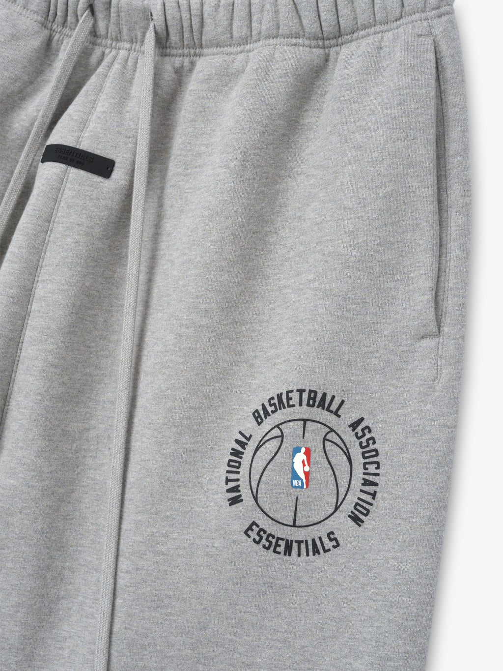 close-up of light gray heavyweight cotton fleece sweatpants with NBA Essentials basketball logo and elastic waistband detail