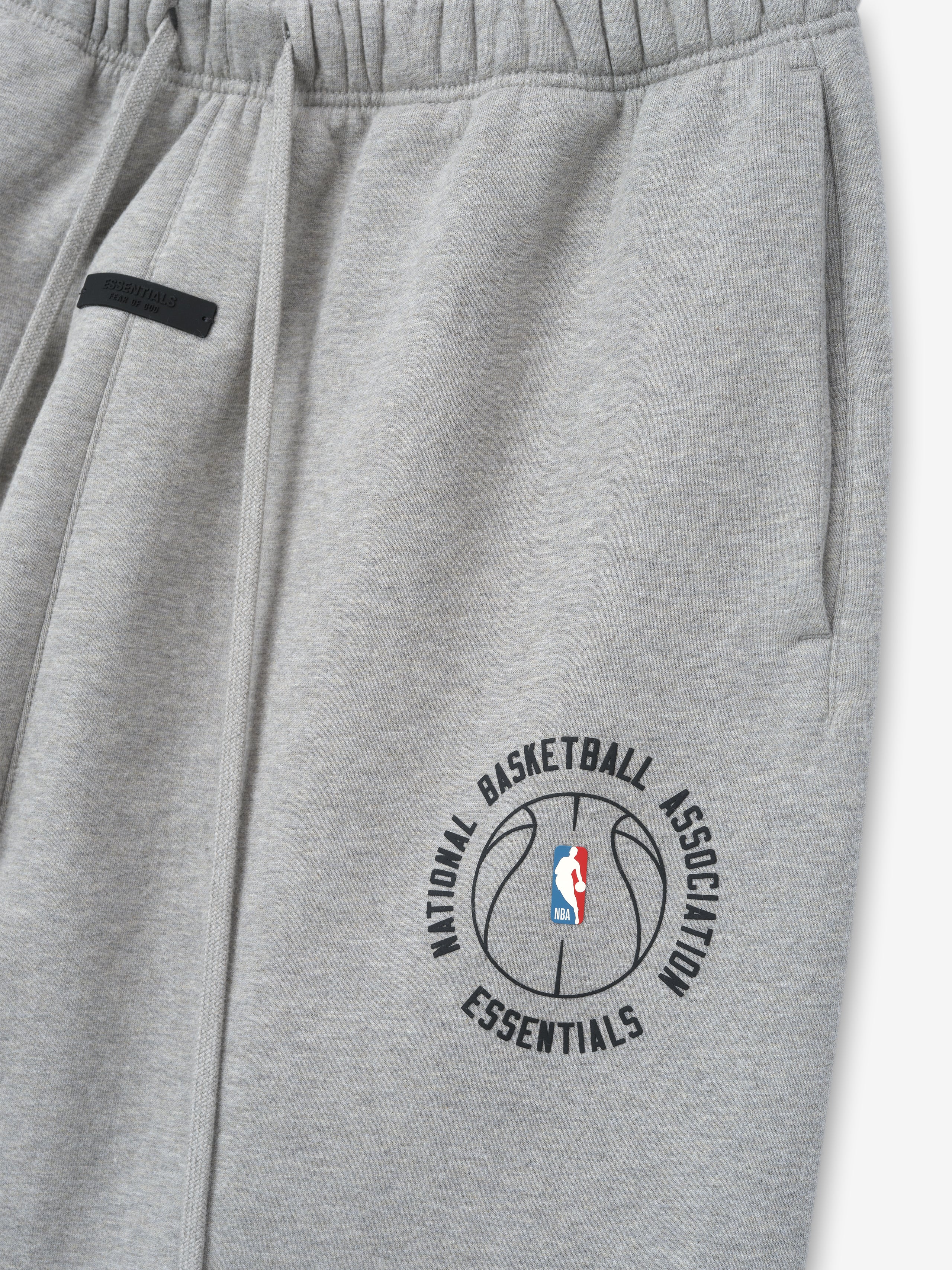 close-up of light gray heavyweight cotton fleece sweatpants with NBA Essentials basketball logo and elastic waistband detail