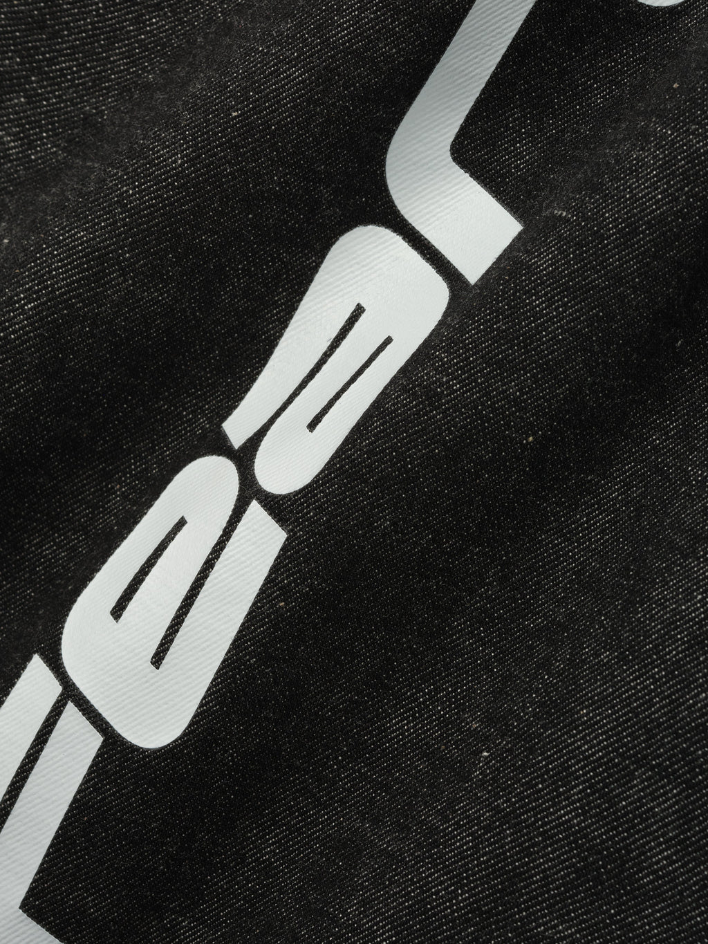Close-up of vintage black denim work pant fabric with partial white graphic print detail on thigh area