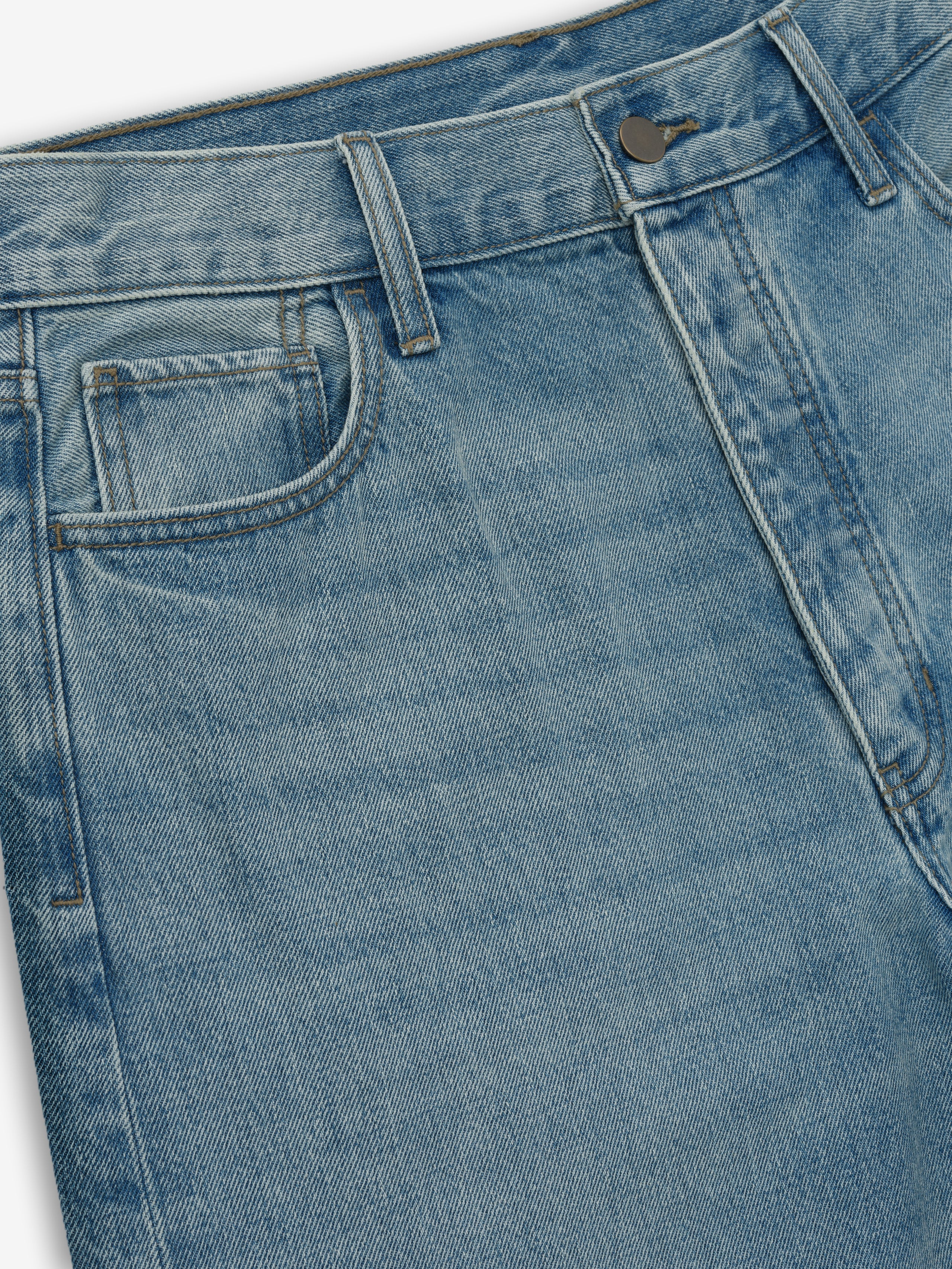 close-up of vintage wash cotton denim jeans with straight leg and classic 5-pocket design with brass button detail