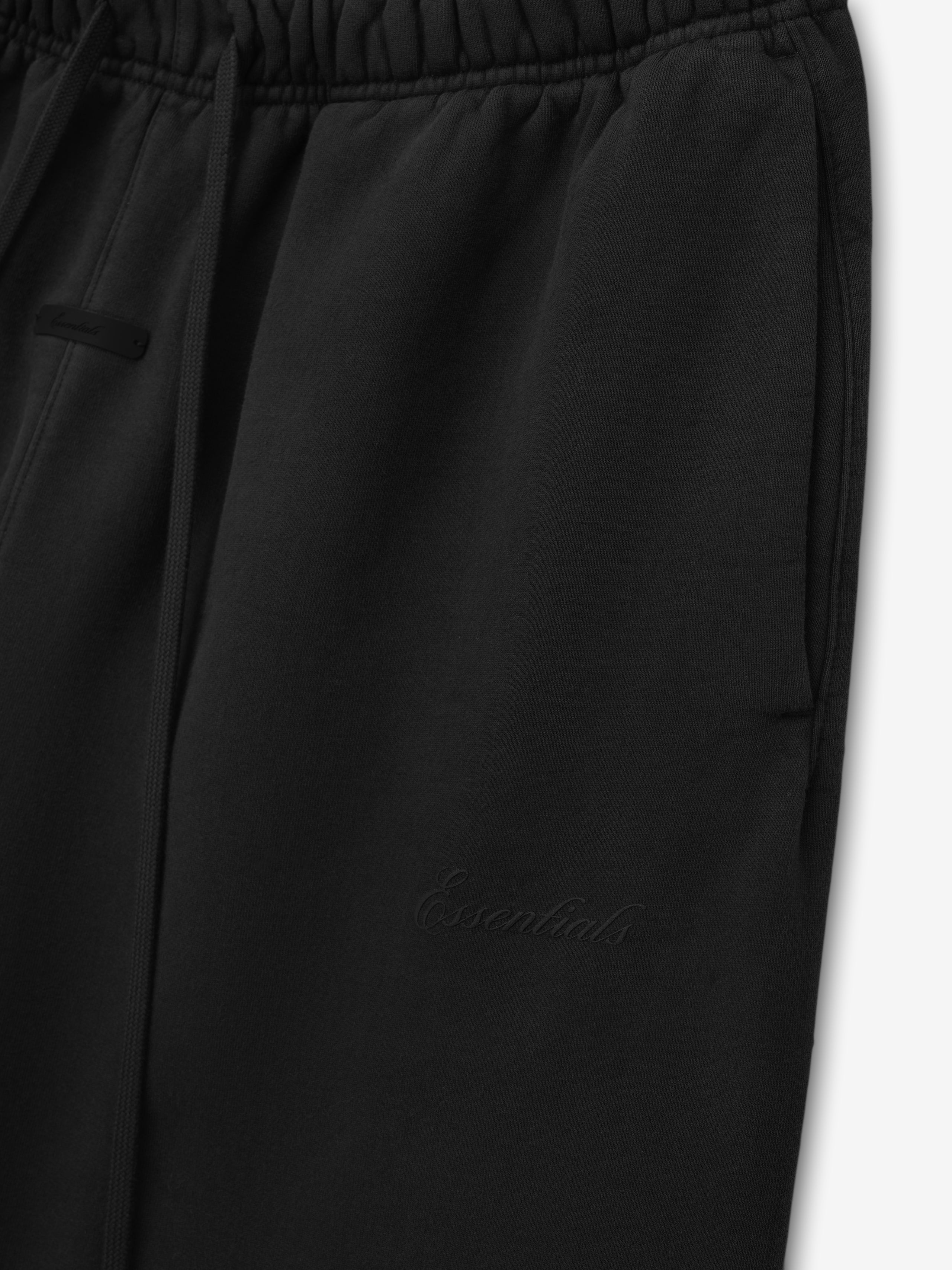 close-up of black heavyweight fleece sweatpants with elastic waistband, drawstring, side pockets, and tonal Essentials logo embroidery