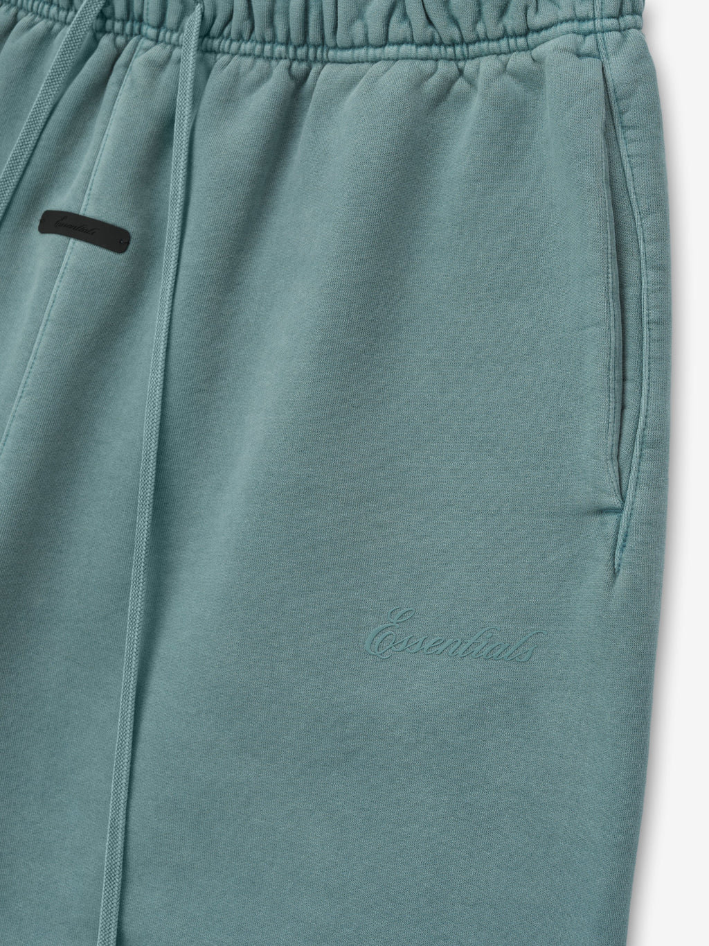 close-up of teal heavyweight fleece sweatpants with elastic waistband, drawstrings, side pockets, and tonal Essentials embroidery