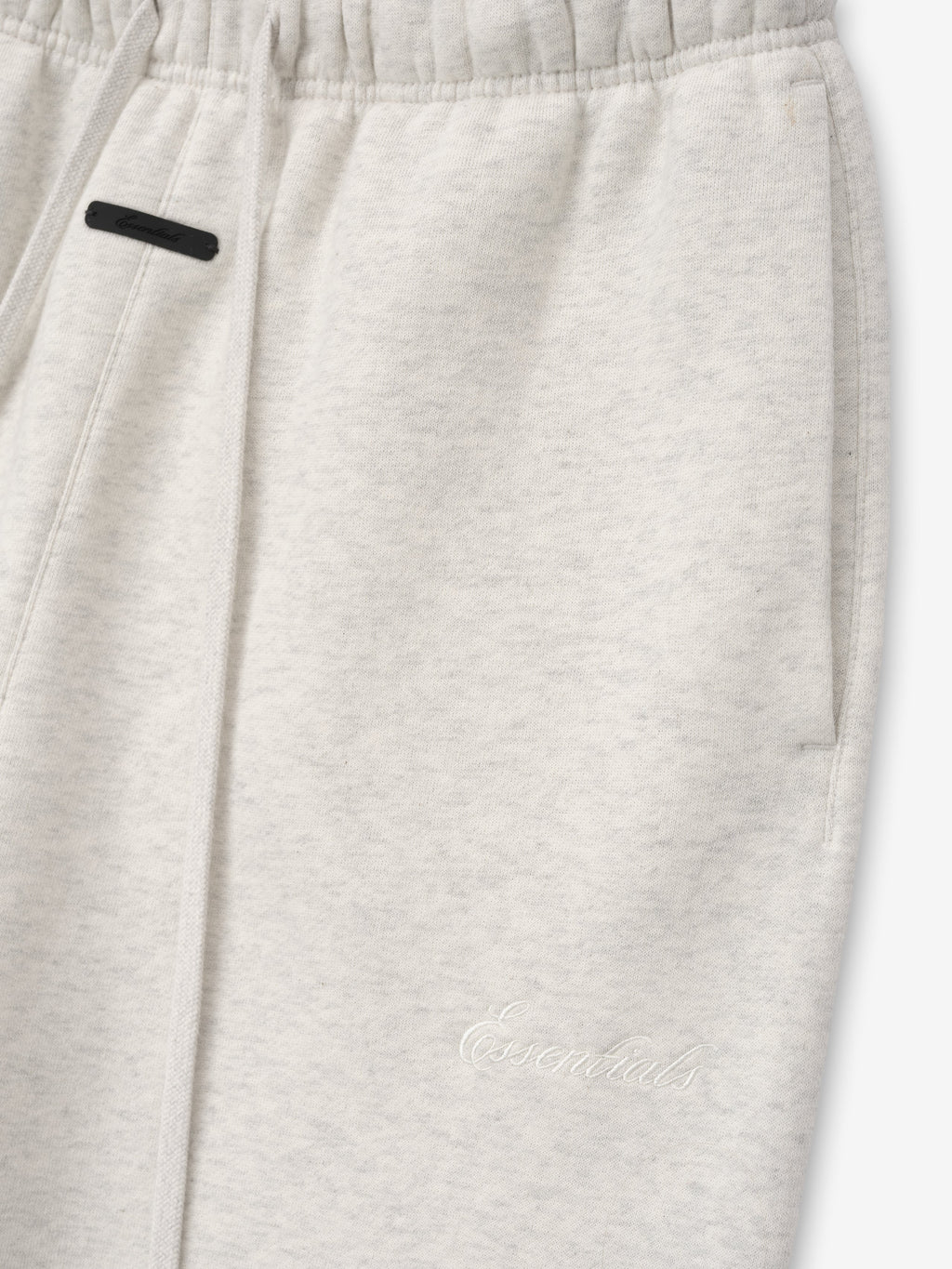 Close-up of light gray sweatpants with a small black label on a white background