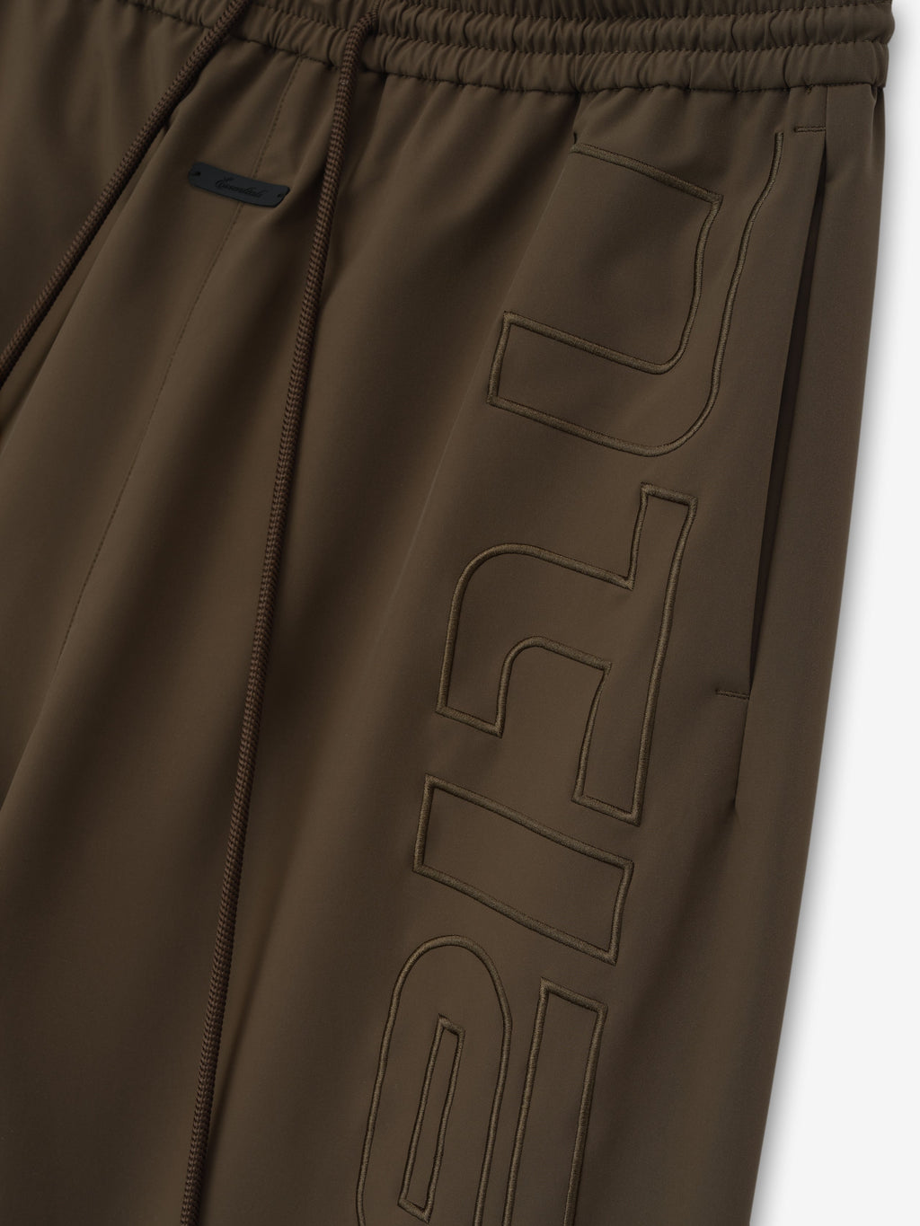 close-up of brown polyester women's track pants with elastic waistband and tonal stitched branding detail on leg