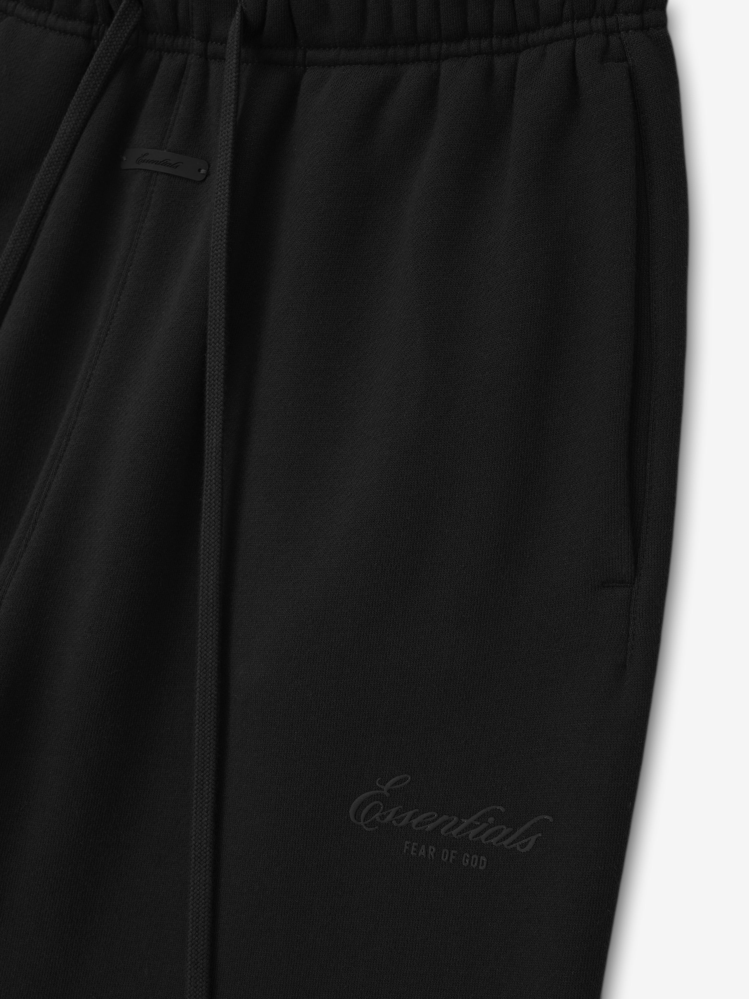 close-up of black core fleece sweatpants with elastic waistband, tapered leg, and embroidered Essentials Fear of God logo