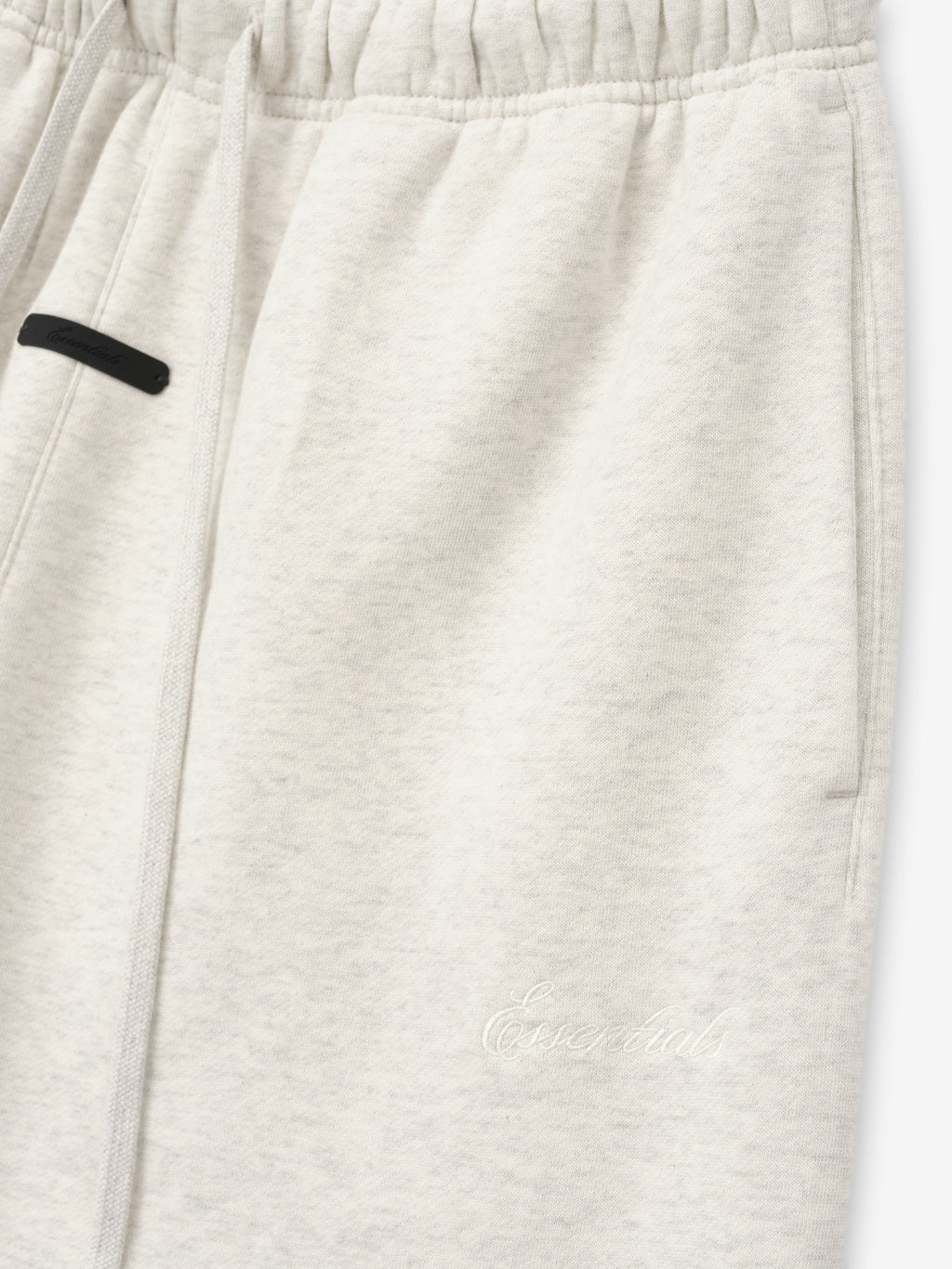 close-up of off-white relaxed flare sweatpants with elastic waistband and tonal Essentials embroidered logo on leg
