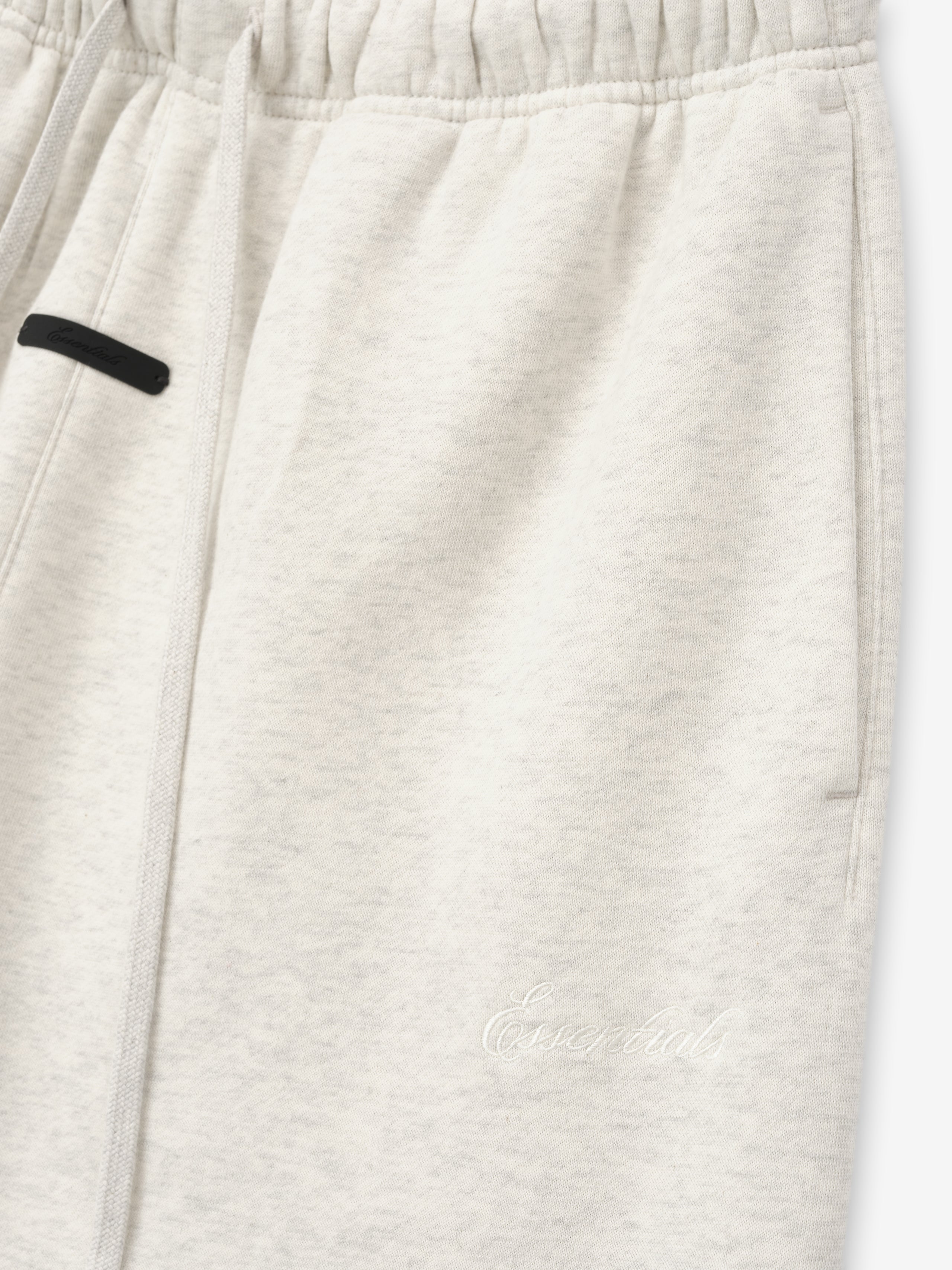 close-up of off-white relaxed flare sweatpants with elastic waistband and tonal Essentials embroidered logo on leg