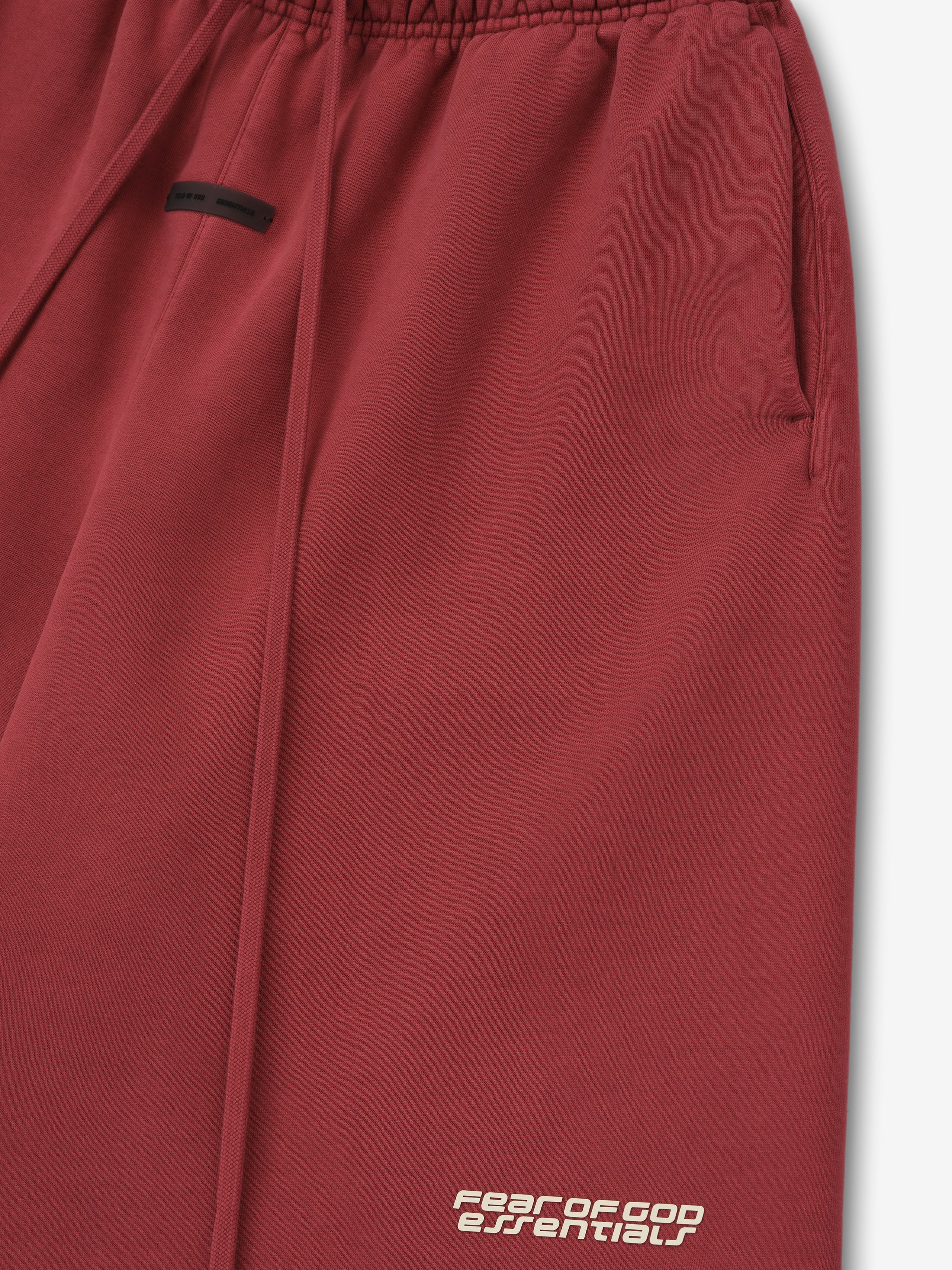 Close-up of crimson relaxed sweatshort with elastic waistband, side pocket, long drawstrings, and logo near hem on white background