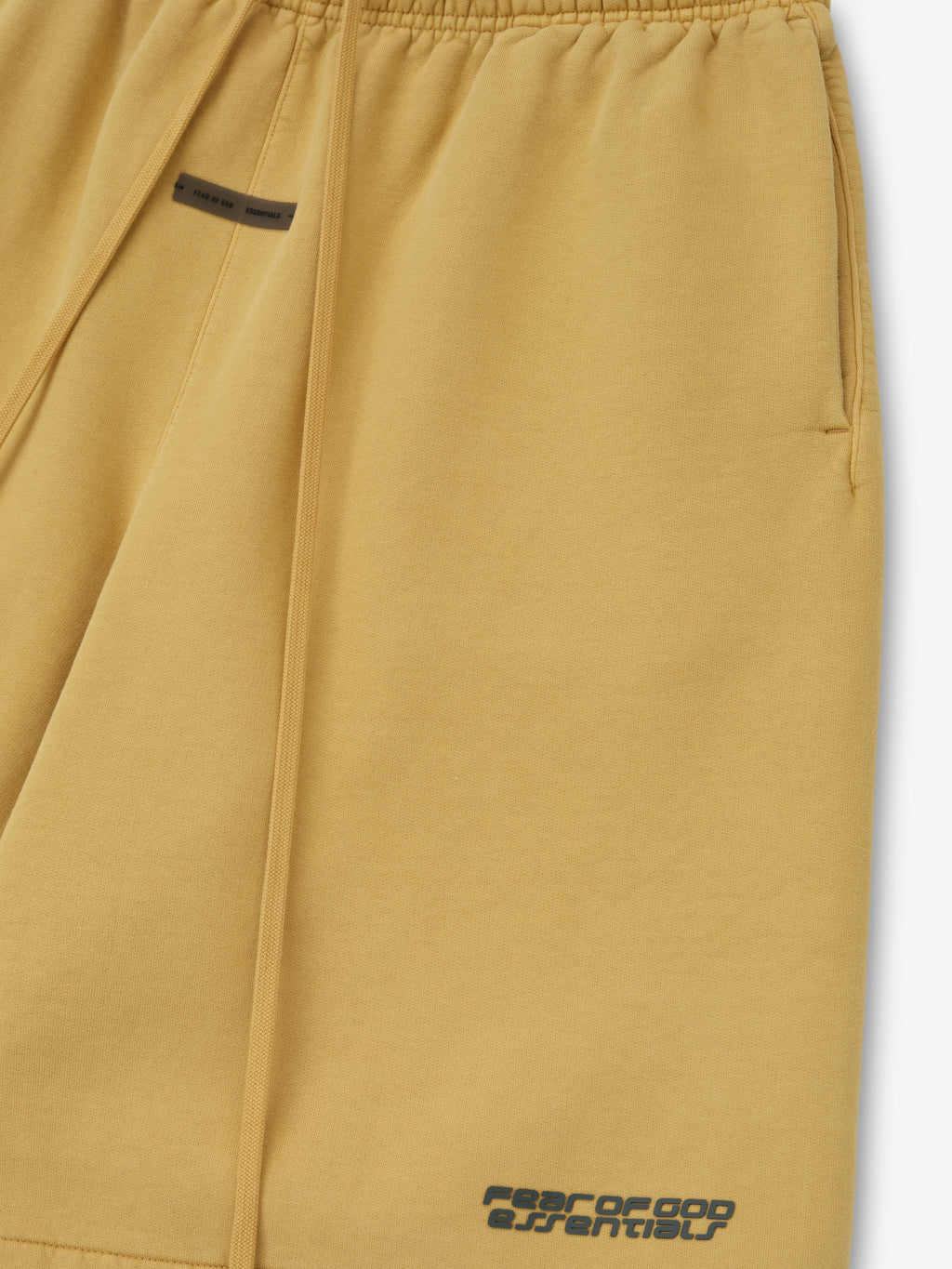 Close-up of relaxed sweatshort in canyon color with elastic waistband, side pocket, long drawstrings, and Fear of God Essentials logo near hem