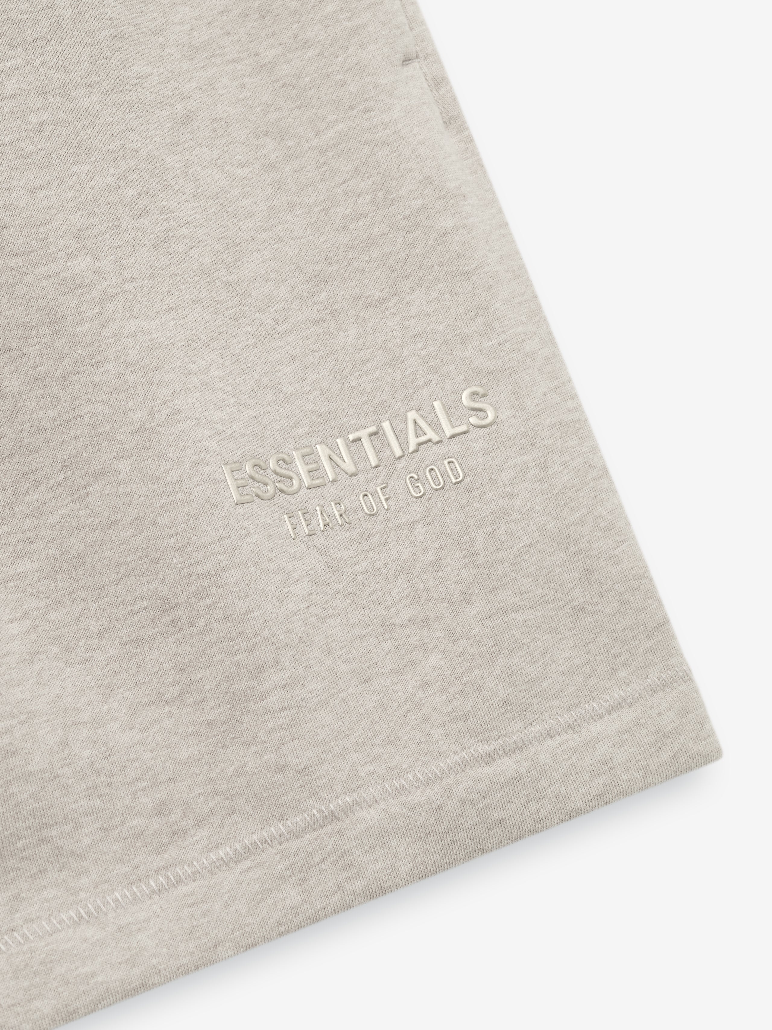 close-up of off-white fleece sweatshort fabric featuring embossed ESSENTIALS Fear of God logo near hem