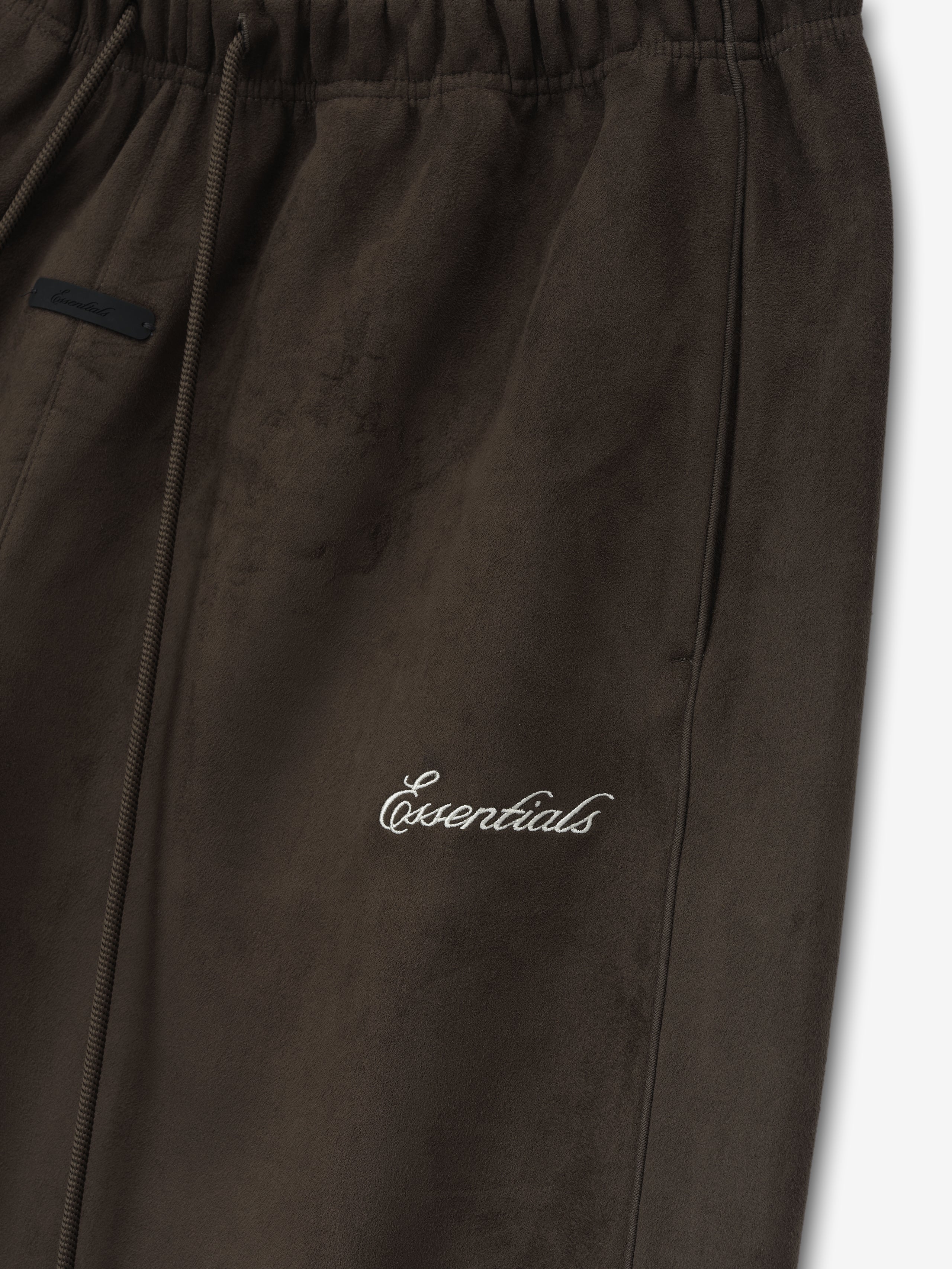 Close-up of dark brown pants with elastic waistband, side pocket, and white cursive "Essentials" embroidery on front leg