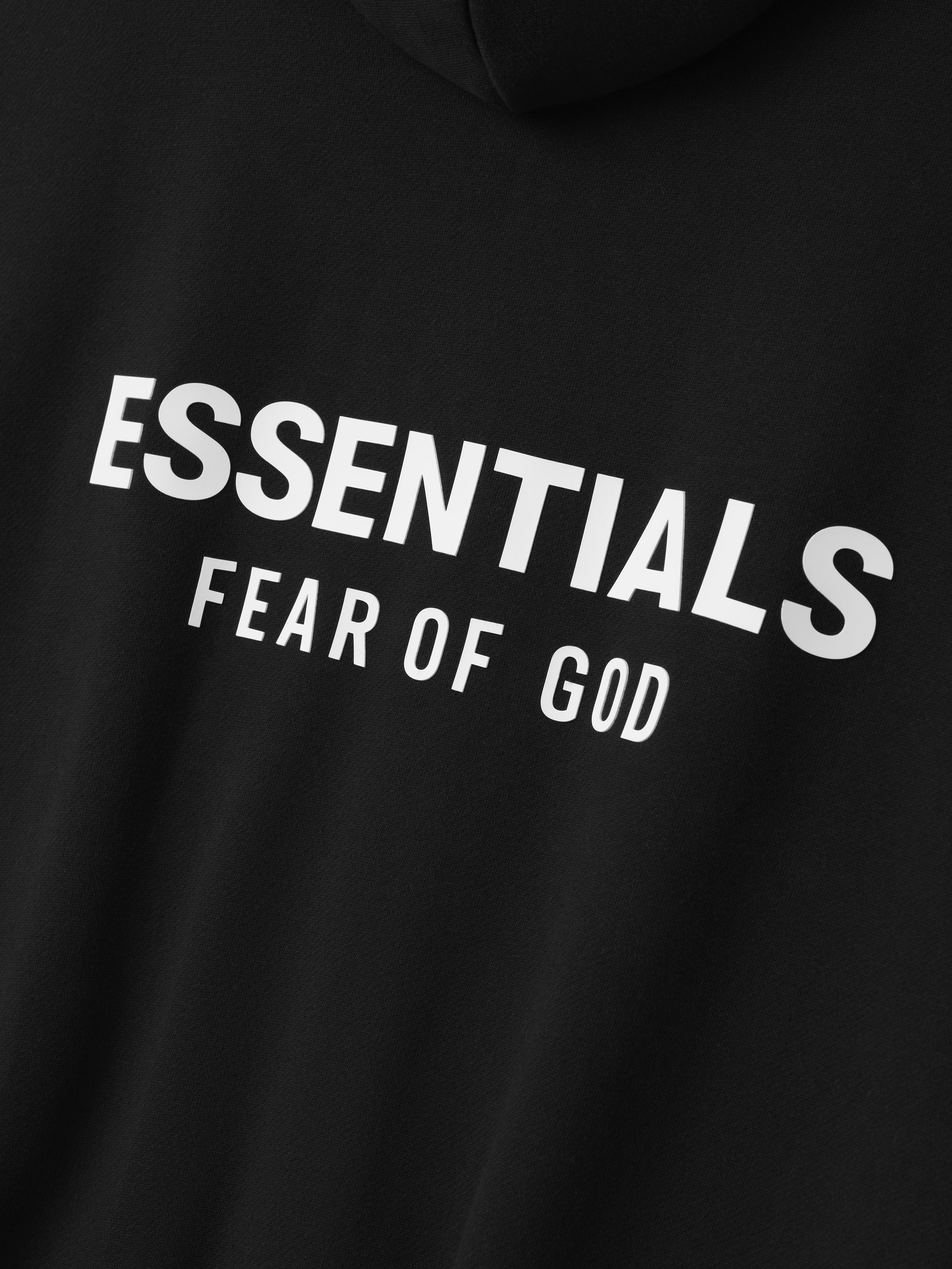 close-up of black hoodie fabric with white Essentials Fear of God logo printed on the back panel
