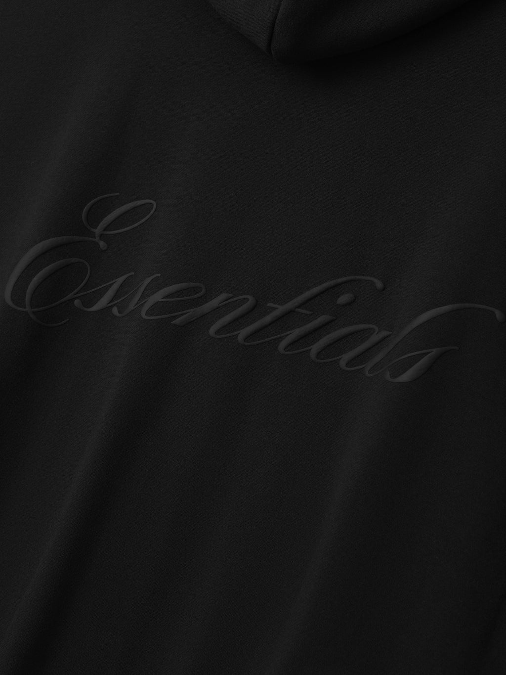 Close-up of black fabric with subtle raised cursive "Essentials" logo printed across the surface