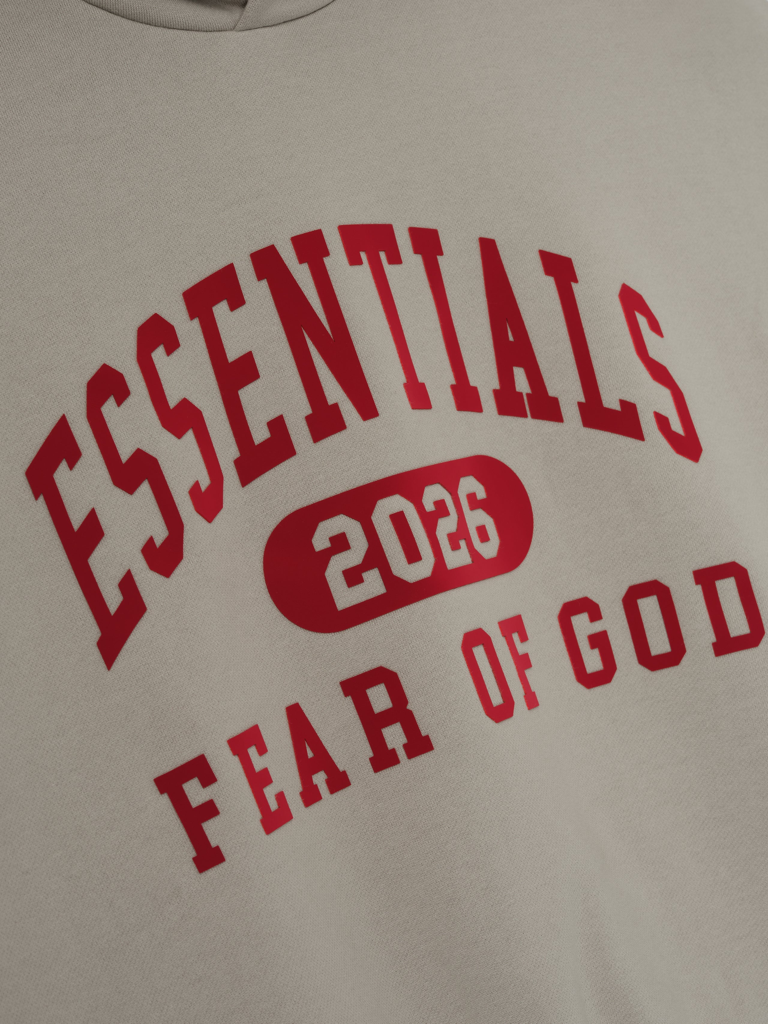 Close-up of smoke grey Classic Hoodie fabric with bold red Essentials 2026 and Fear of God text print detail