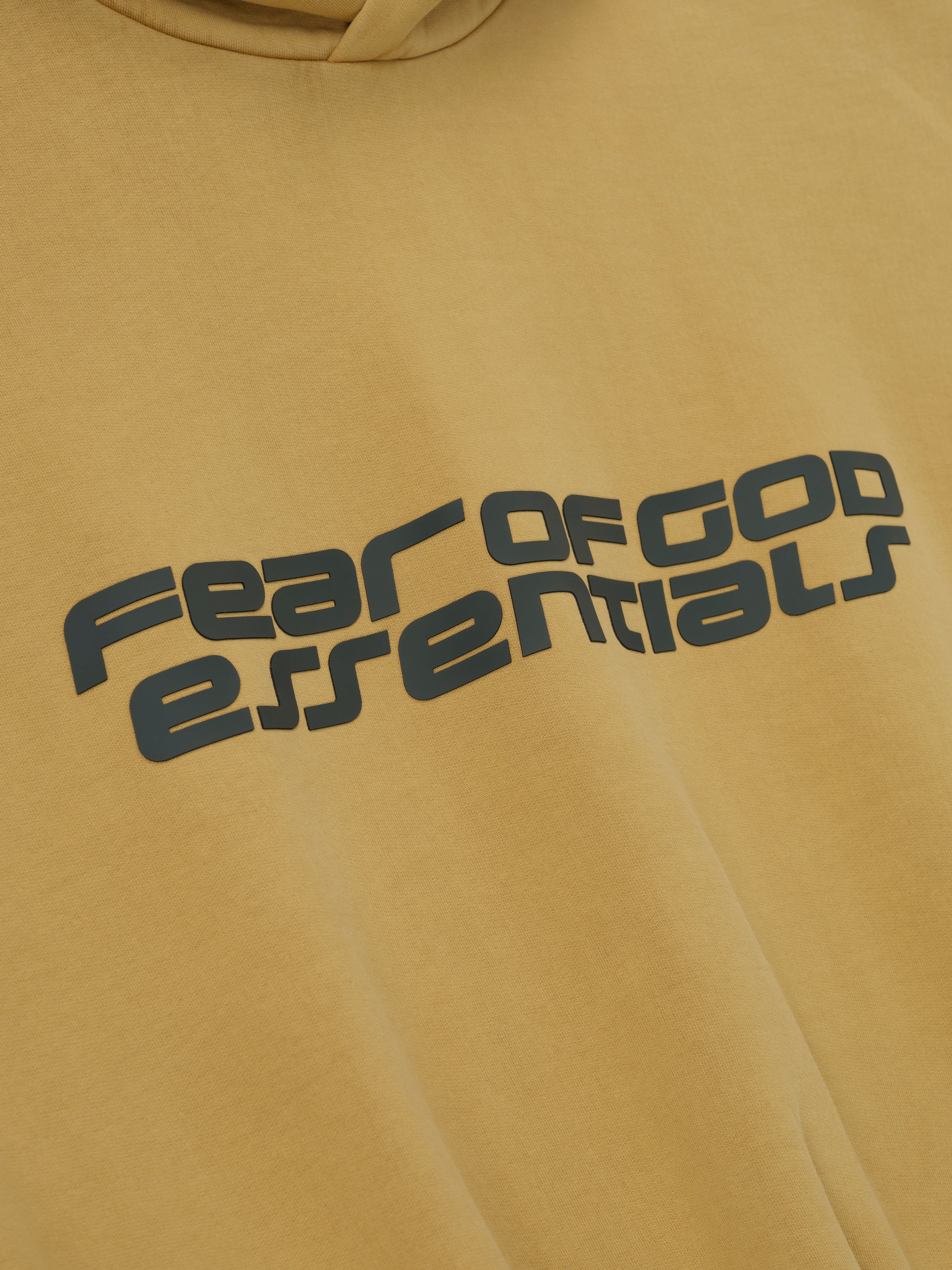 Close-up of canyon-colored cropped relaxed hoodie with large dark grey Fear of God Essentials logo across chest