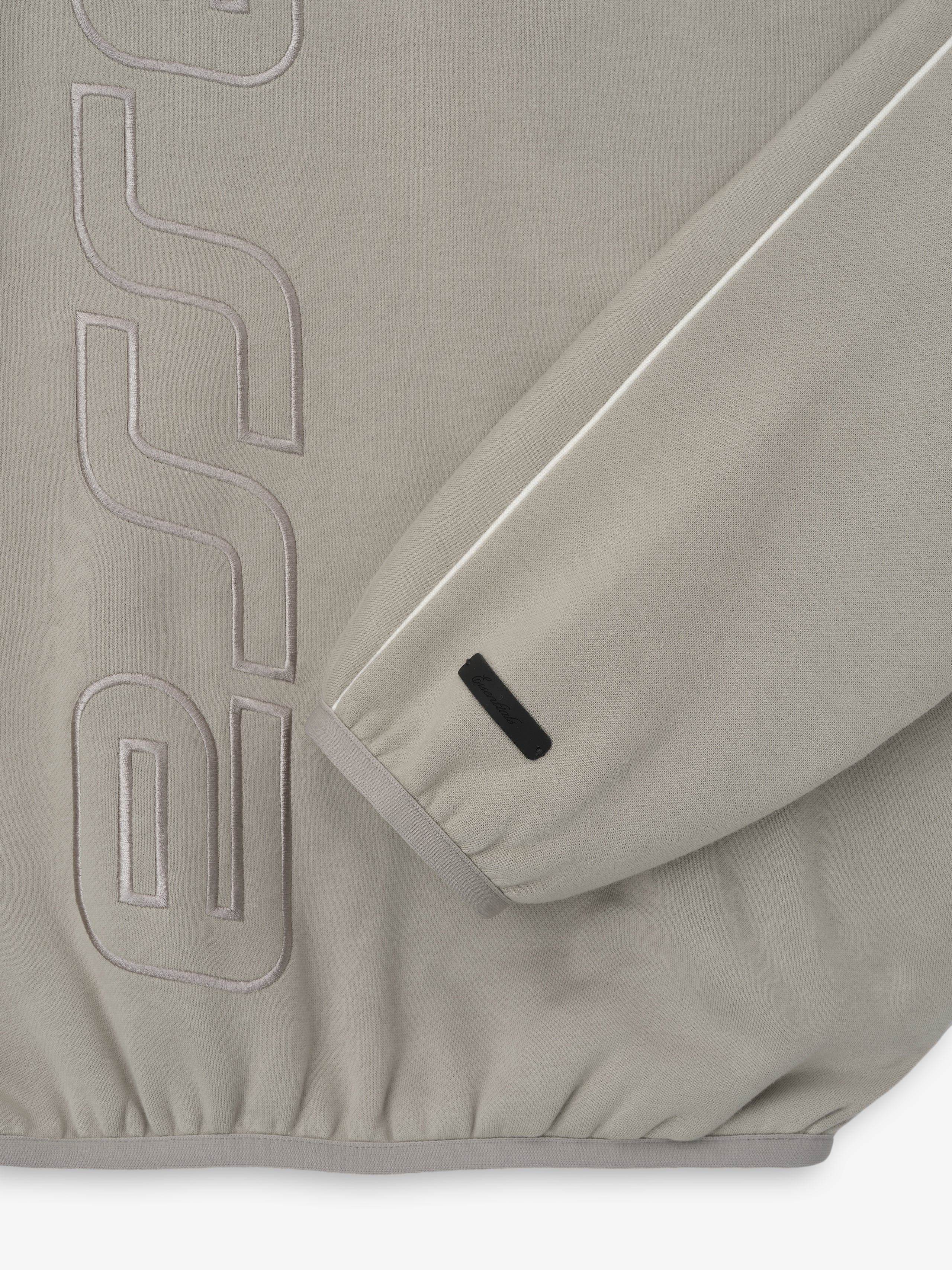 Close-up of light taupe sweatshirt sleeve with white piping and tonal embossed lettering on the body
