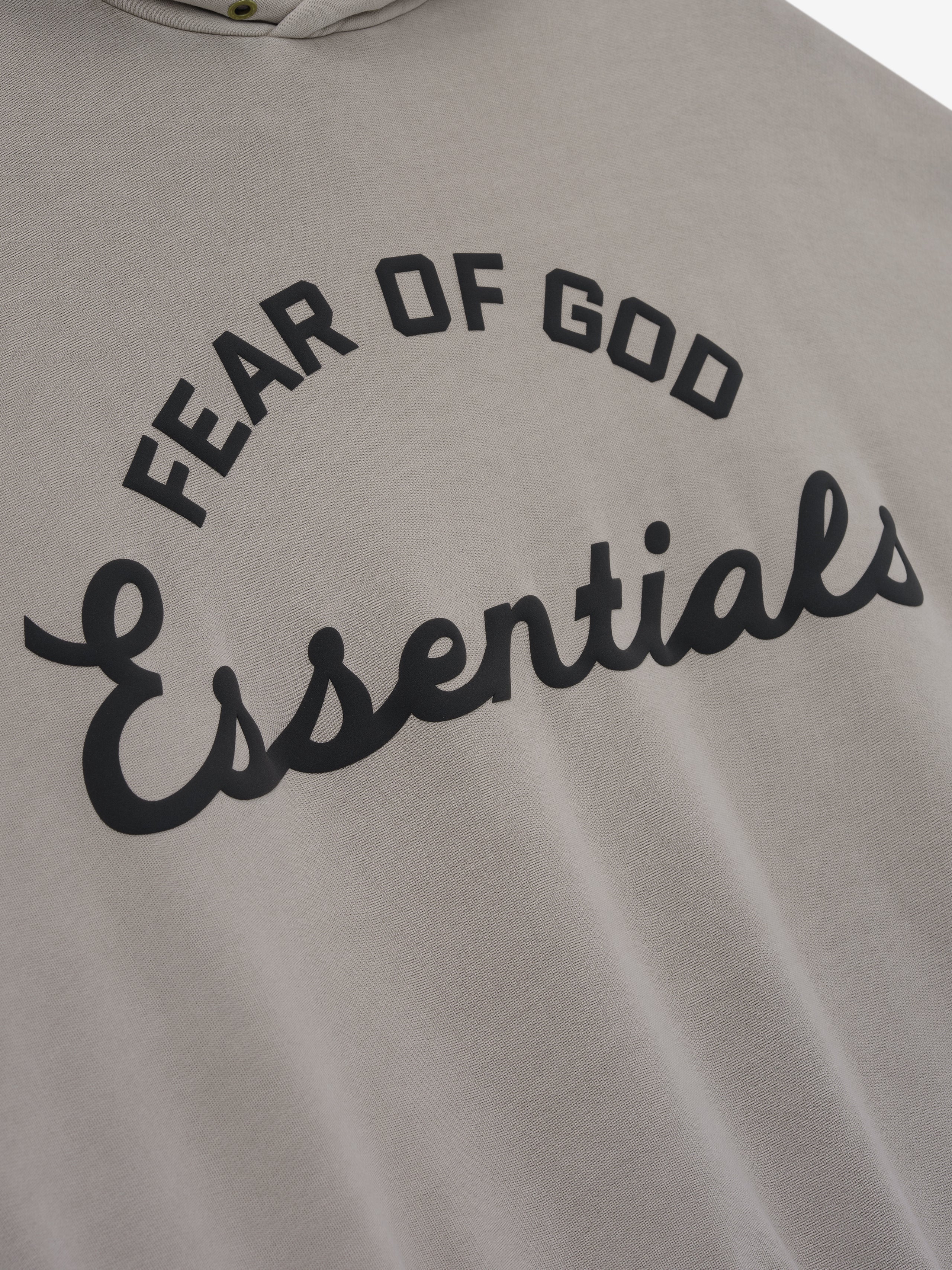 close-up of taupe cotton fleece hoodie with black puff-printed Fear of God Essentials logo on front
