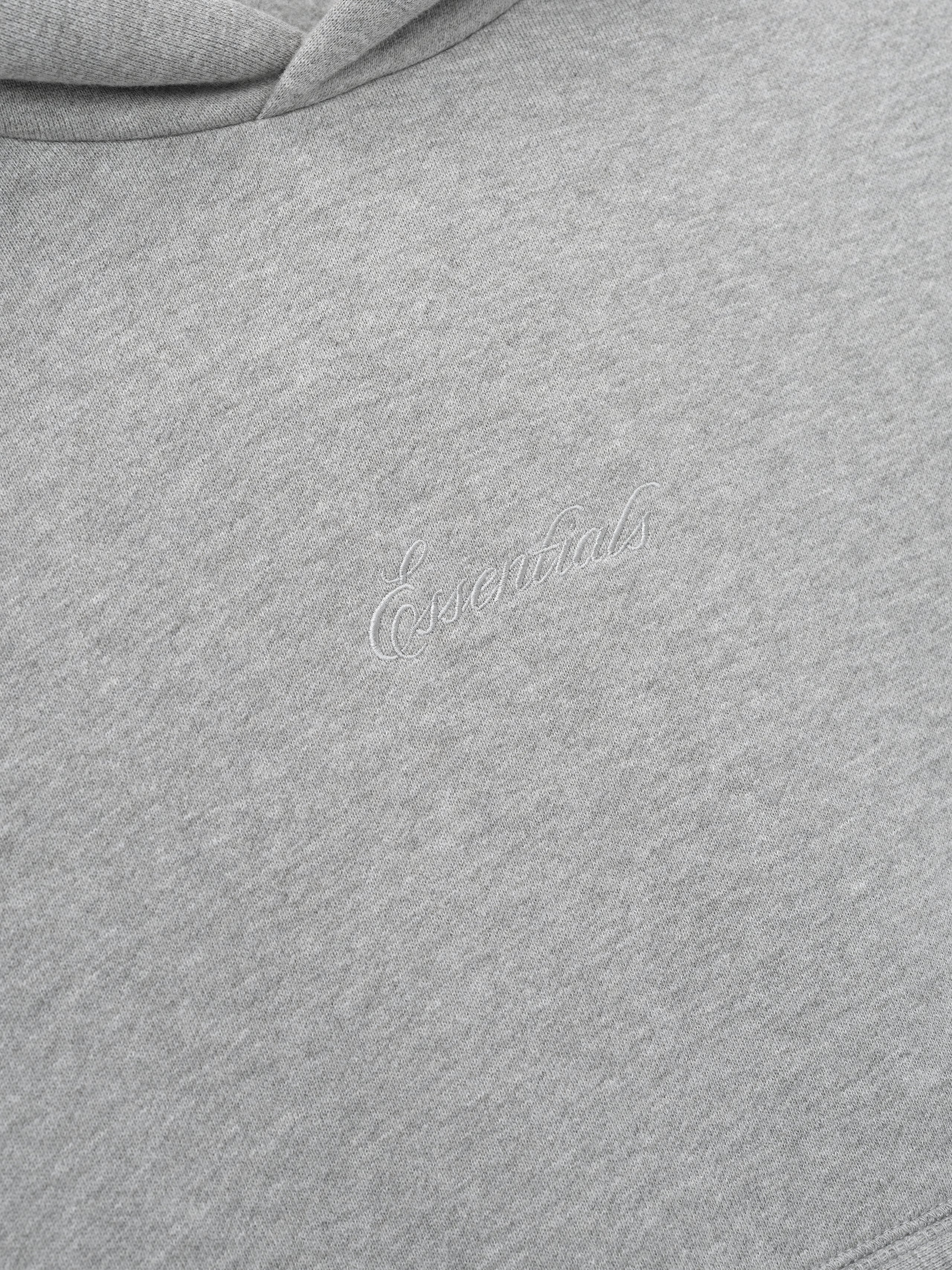 Close-up of a gray hoodie with essentials embroidery script