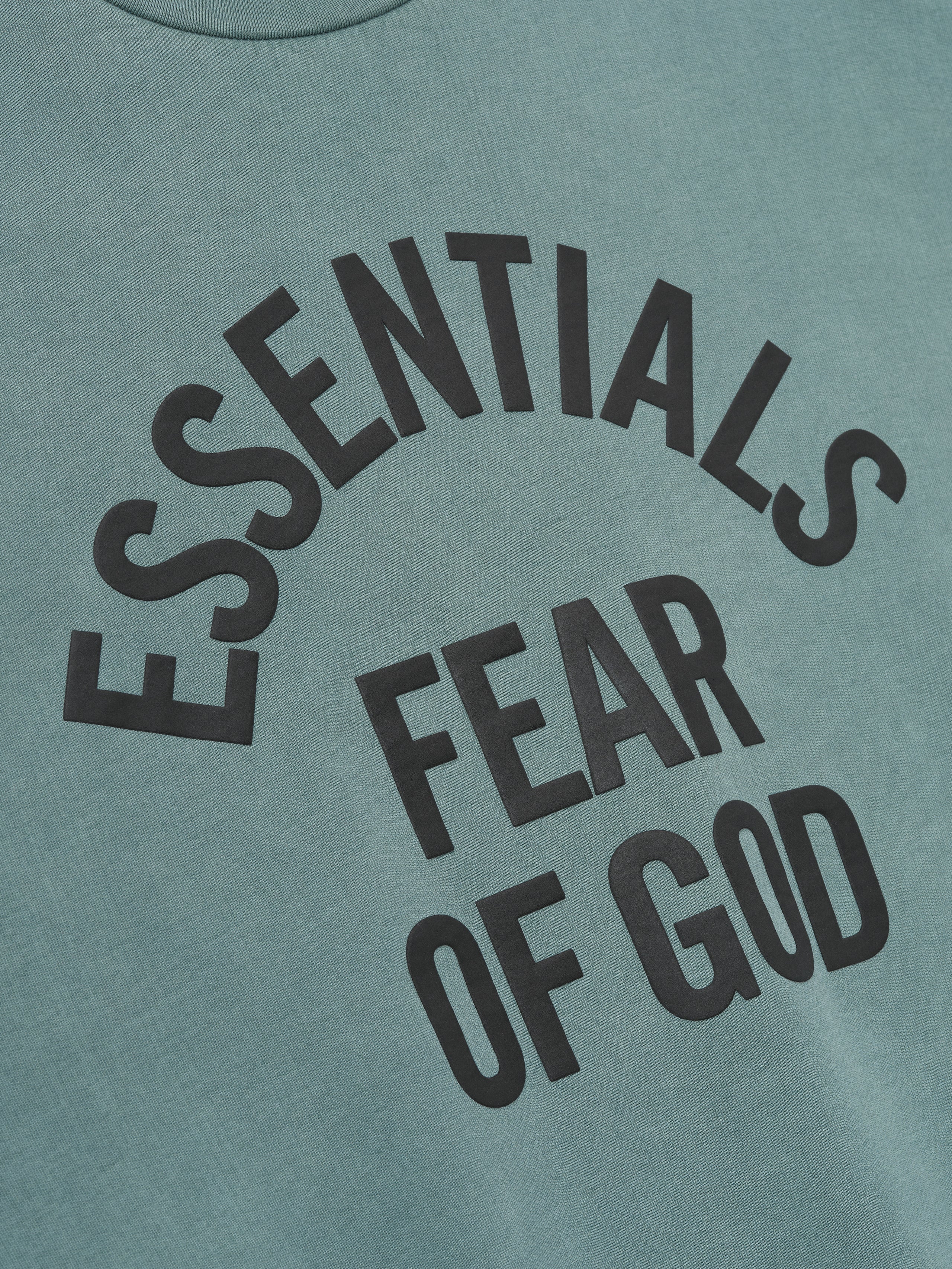 close-up of pigment-dyed teal fabric with large black Essentials Fear of God printed logo on sweatshirt