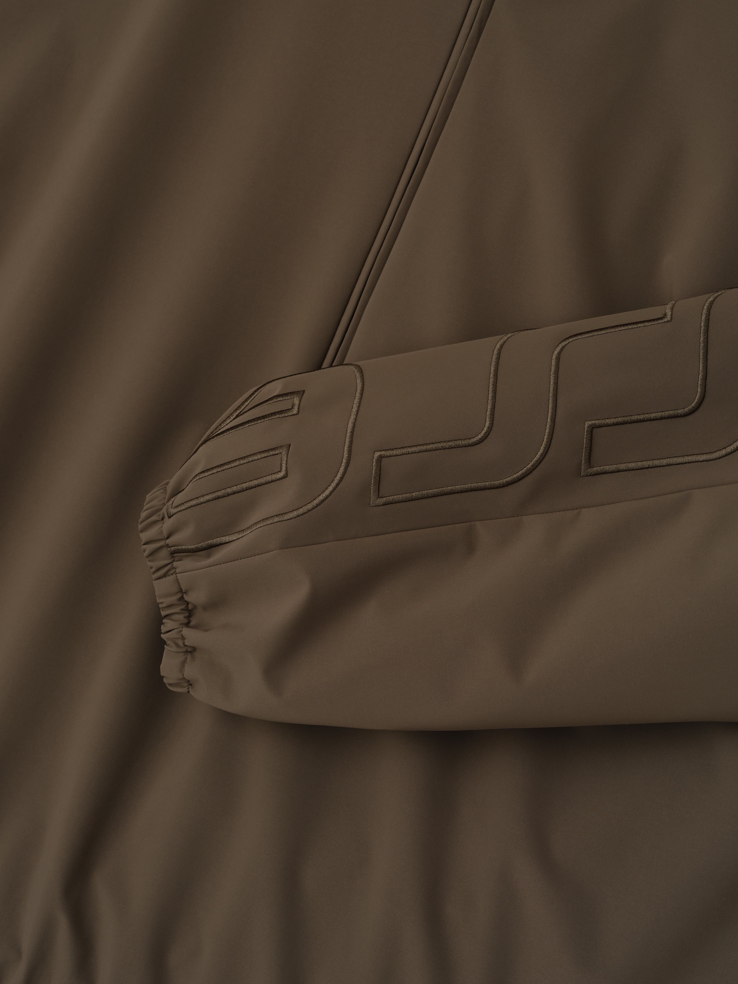 Close-up of a brown jacket with a brand logo on the chest.
