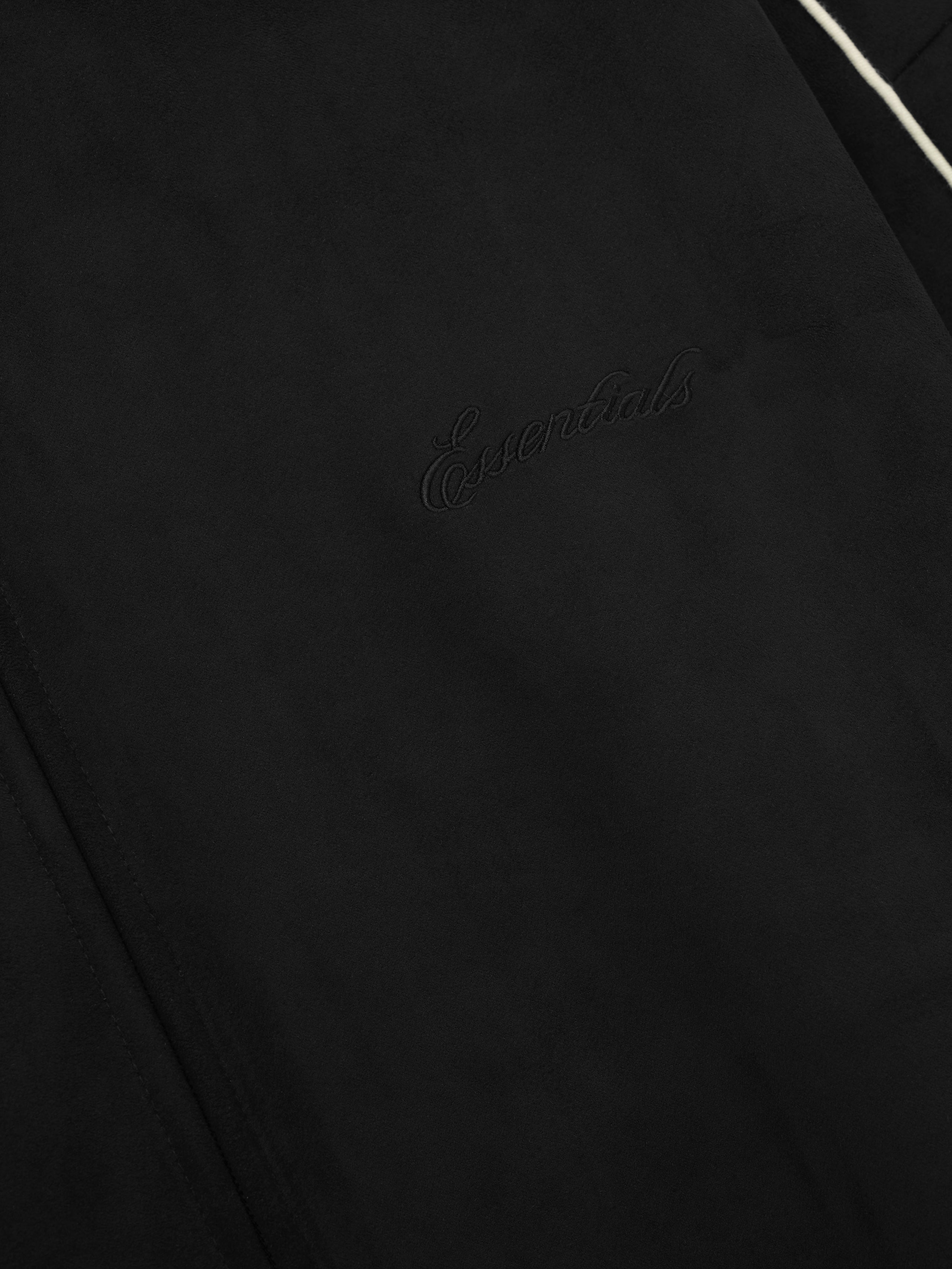 close-up of black bonded suede fleece fabric with subtle embossed Essentials logo and white piping detail