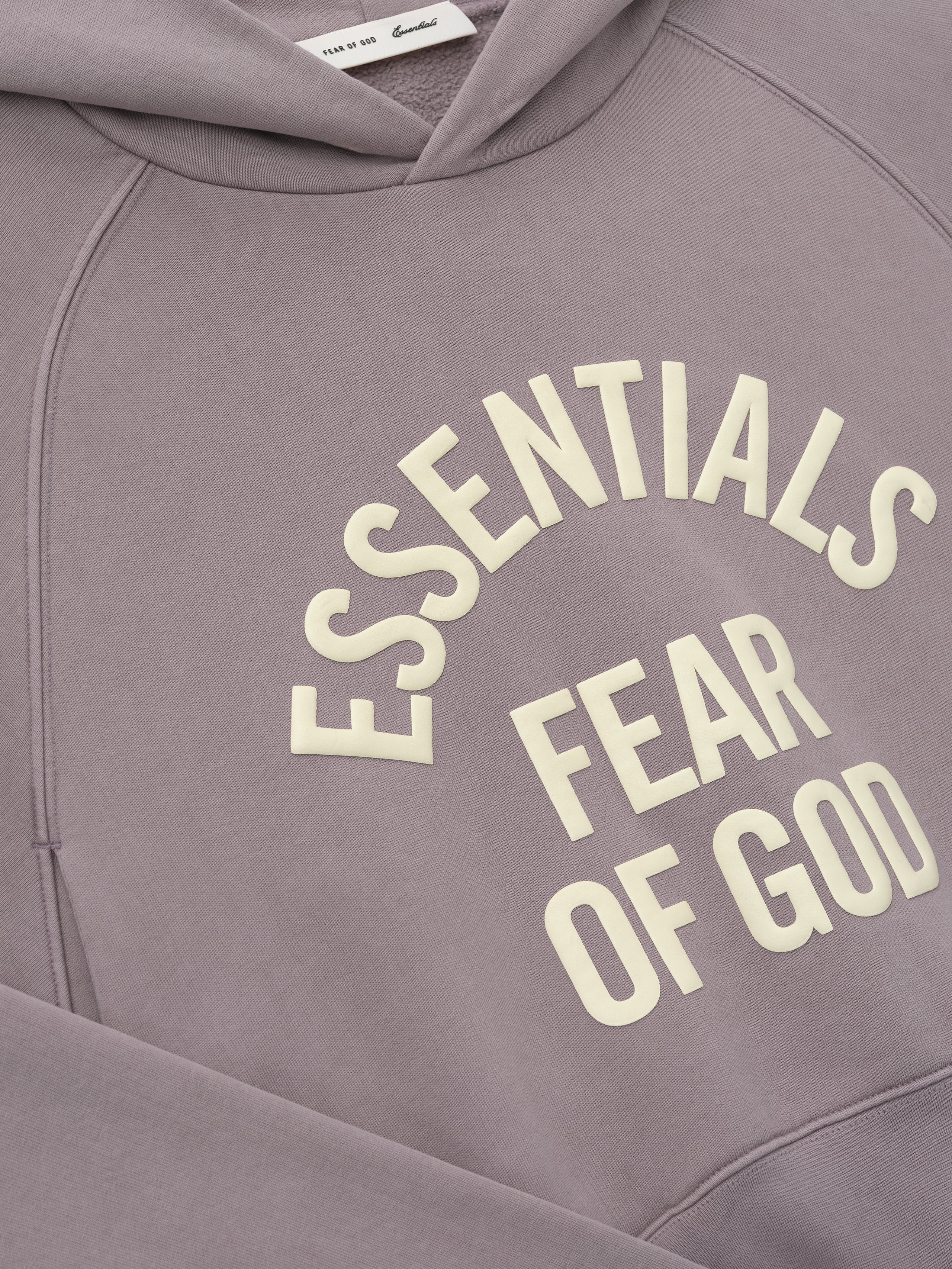 Close-up of mauve hoodie with cream "ESSENTIALS FEAR OF GOD" text printed in curved layout on front panel
