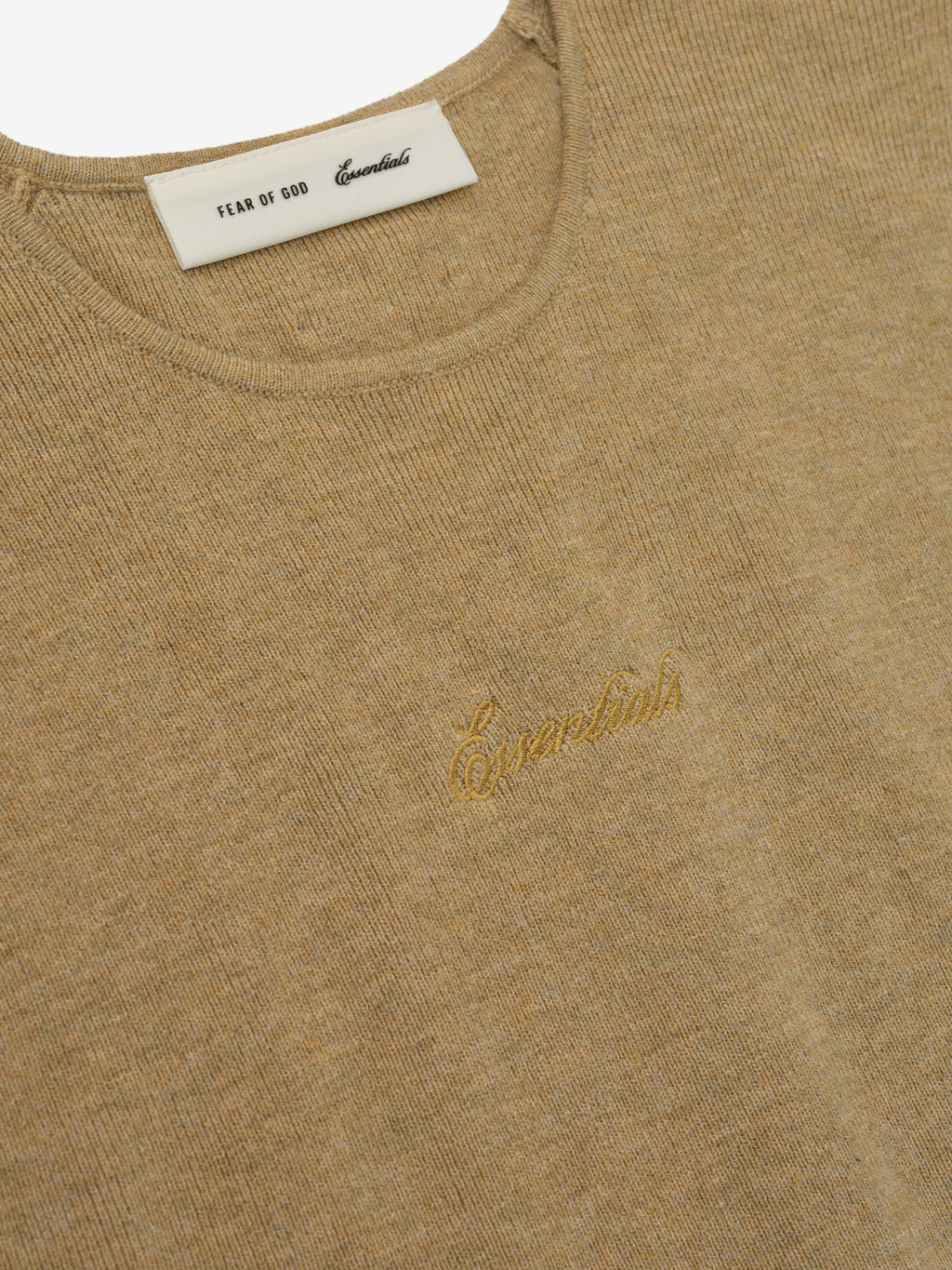 Close-up of a beige sweater with a gold logo and label on a white background