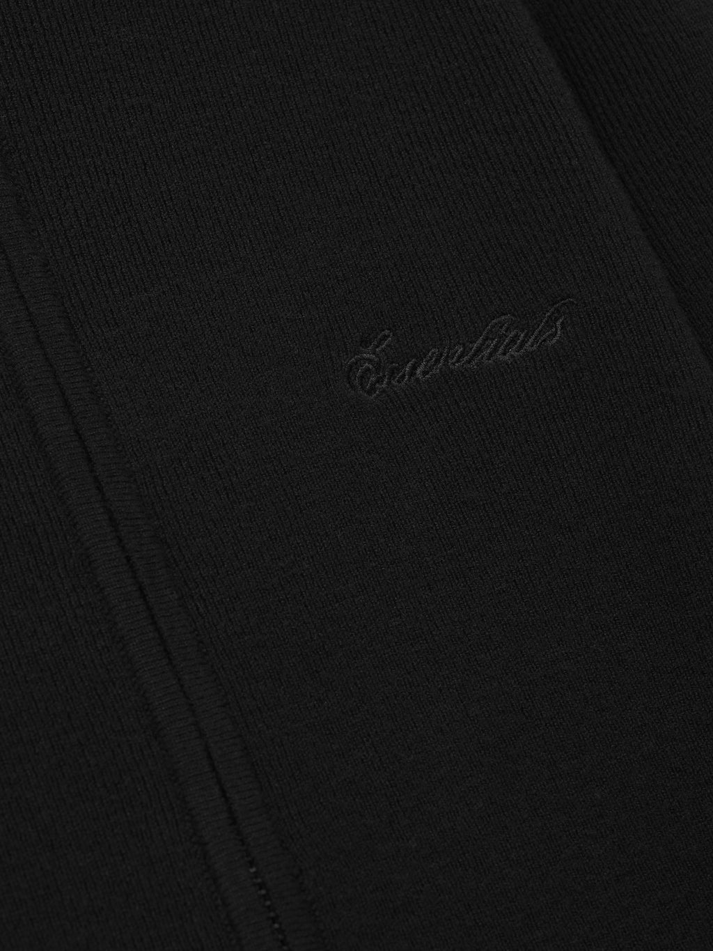 Close-up of a black fabric with 'Essentials' embroidery on a dark background