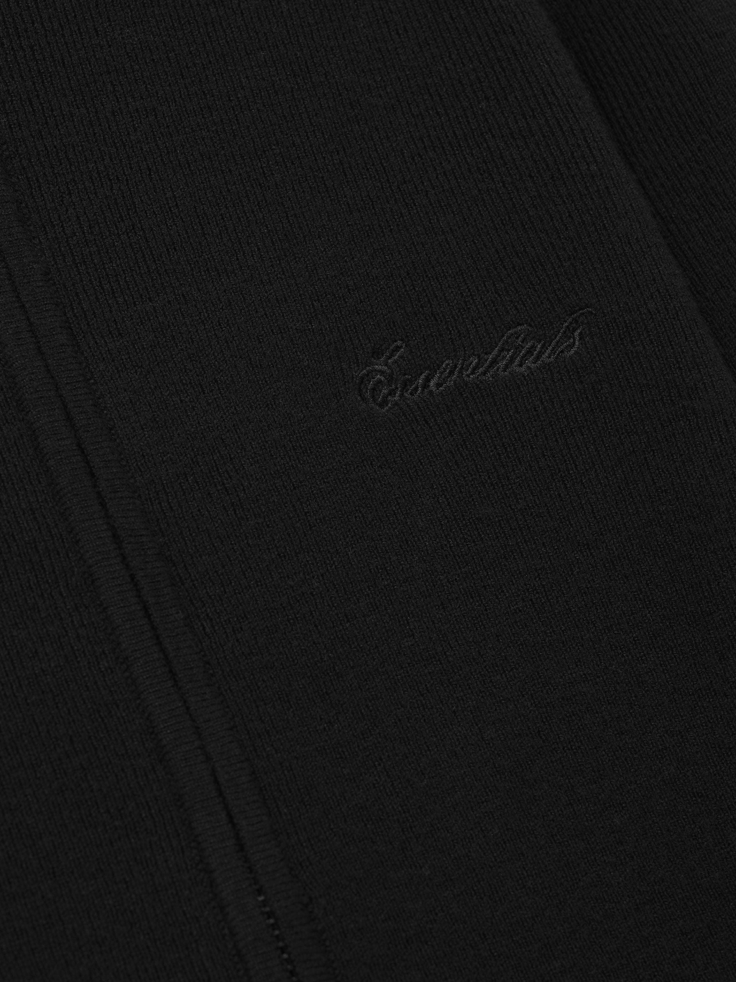 Close-up of a black fabric with 'Essentials' embroidery on a dark background