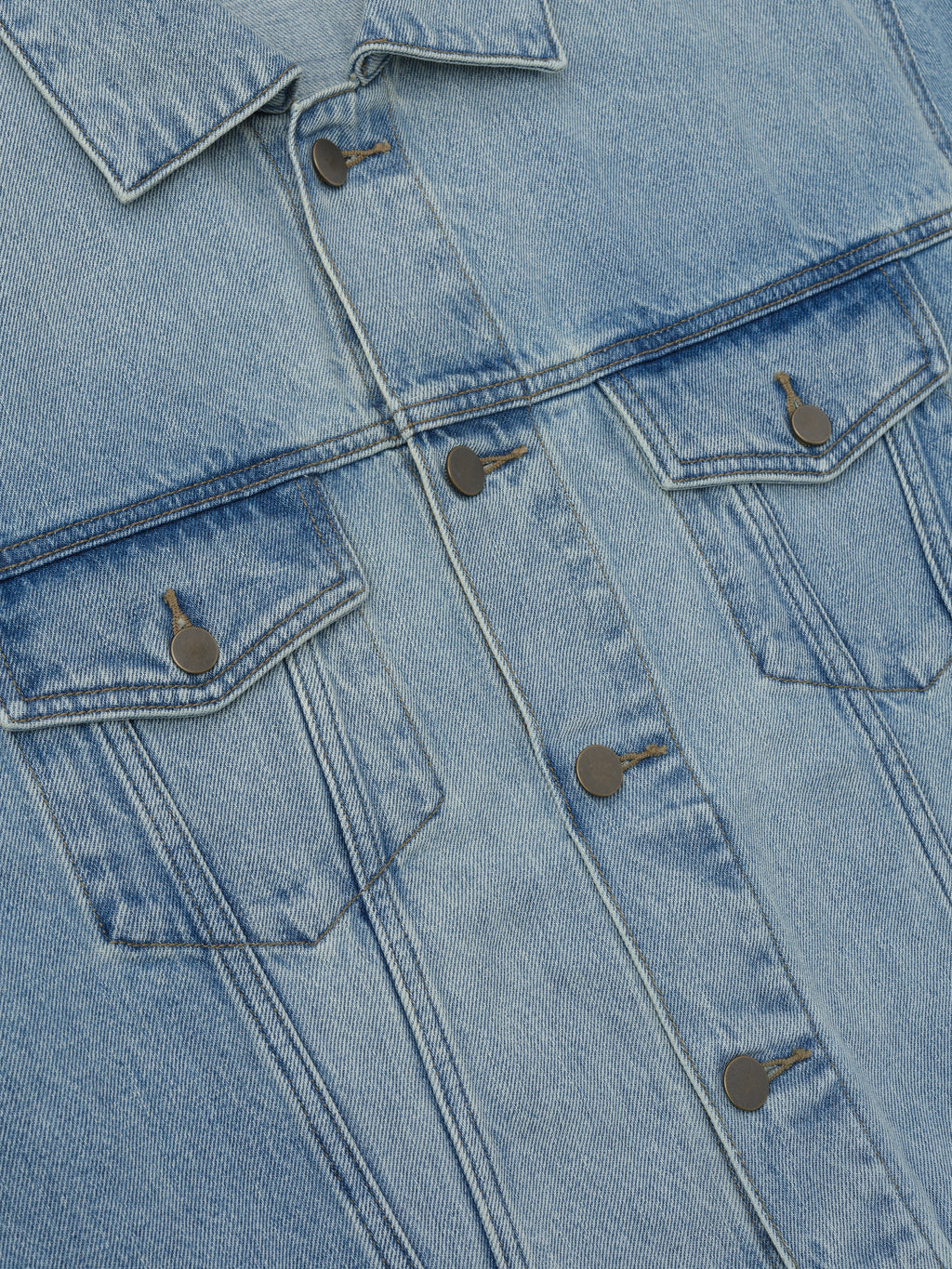 Close-up of light wash denim jacket front with button closures and two flap chest pockets on light background