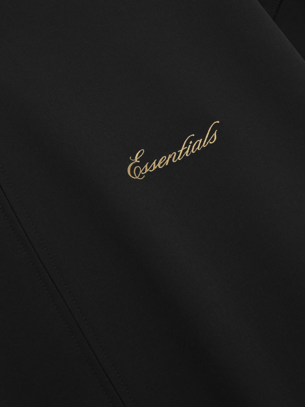 Black fabric with 'Essentials' embroidered in gold on a dark background