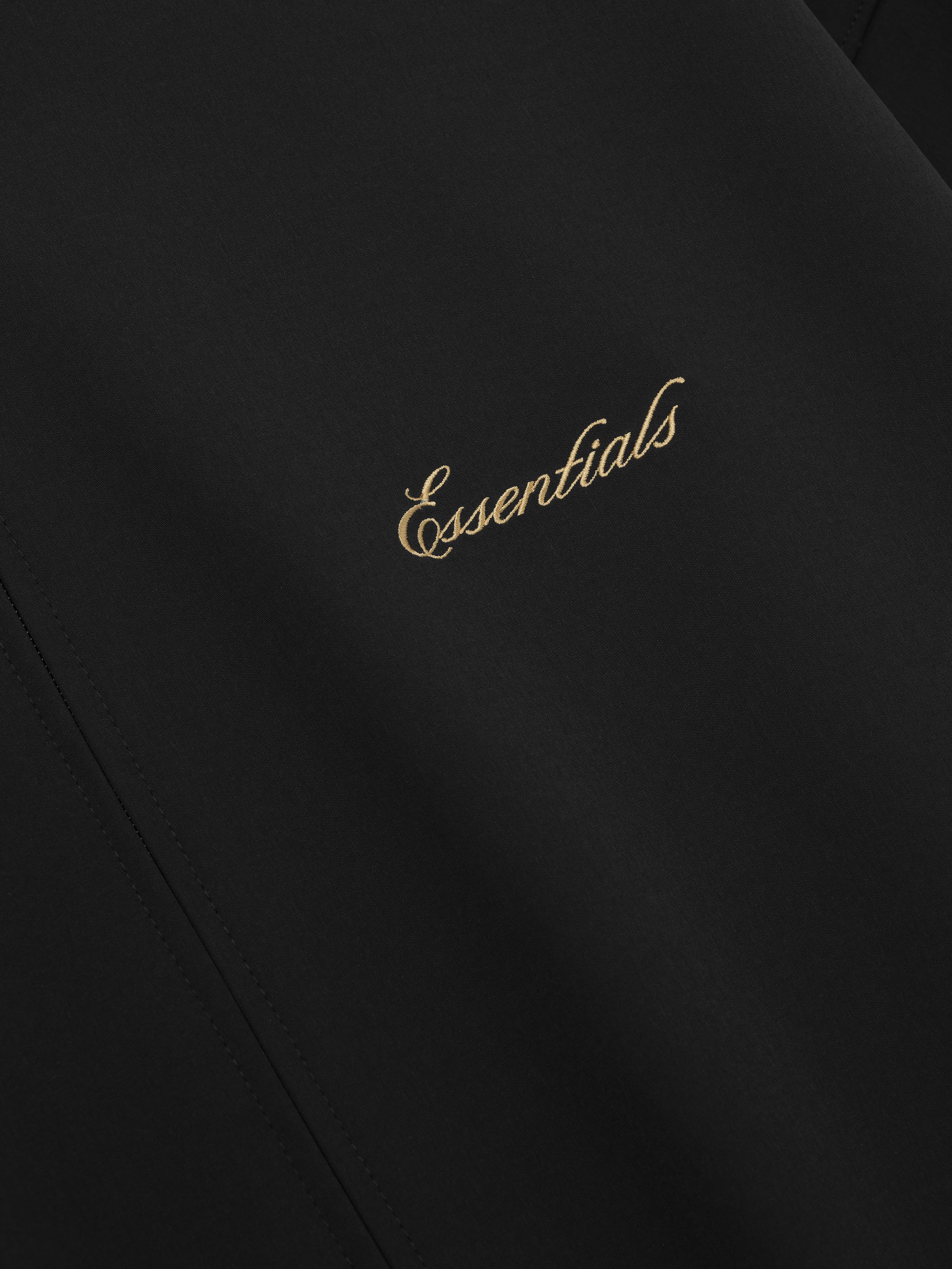 Black fabric with 'Essentials' embroidered in gold on a dark background