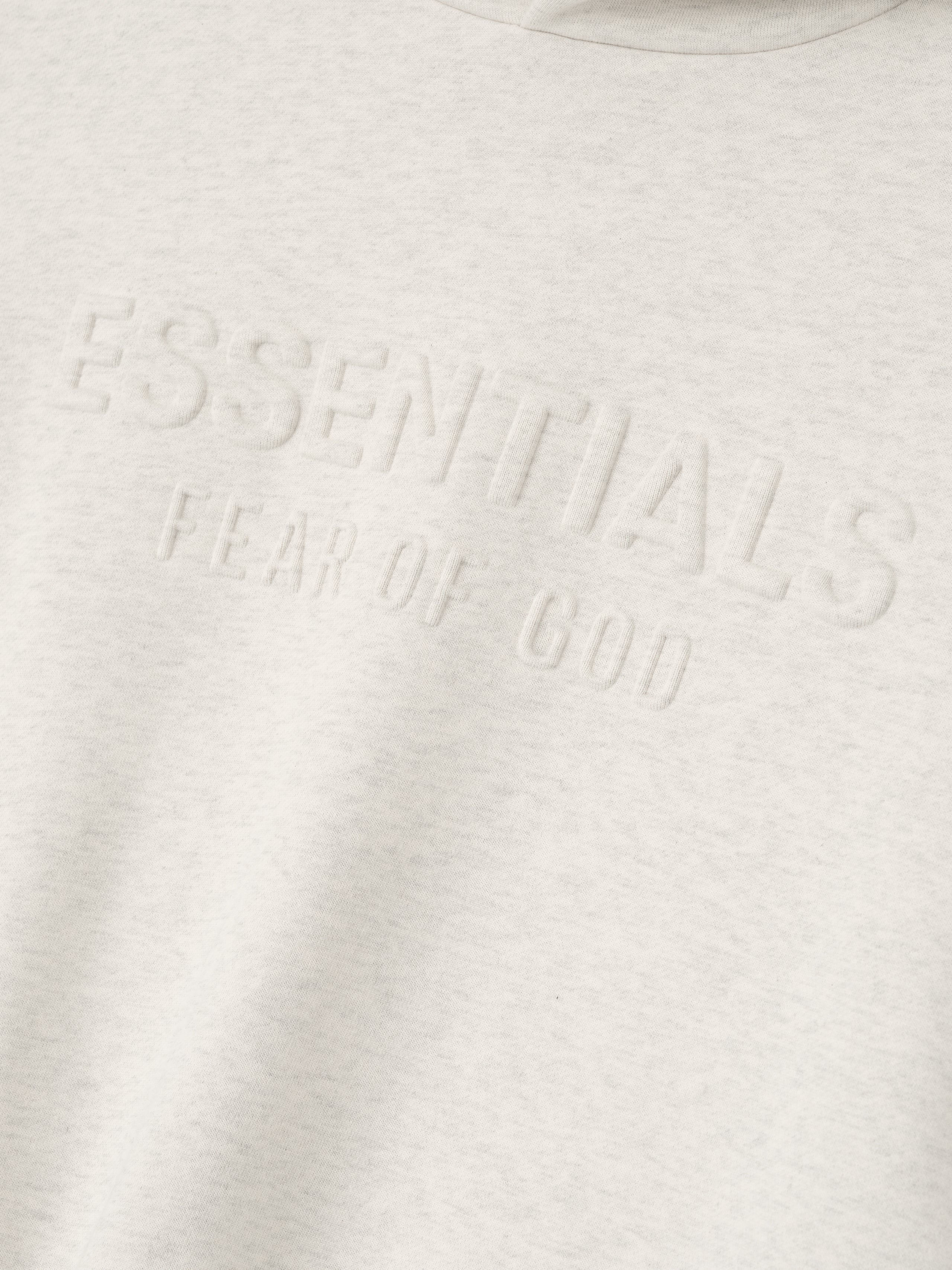 Close-up of oatmeal heather Kids Embossed Classic Hoodie showing raised ESSENTIALS Fear of God text on chest, gallery position 0