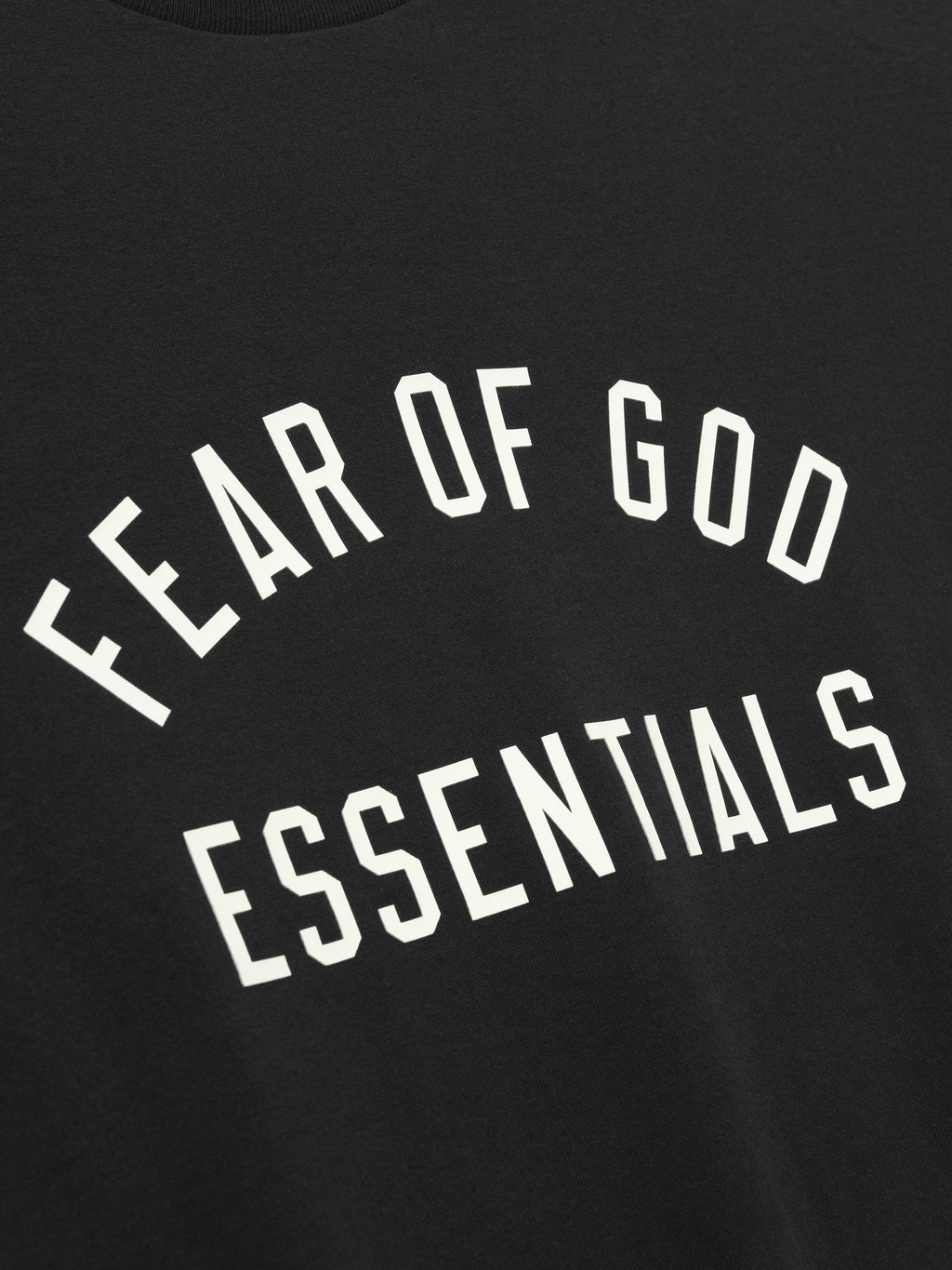 Close-up of black fabric with white "FEAR OF GOD ESSENTIALS" text printed in arched design on front panel