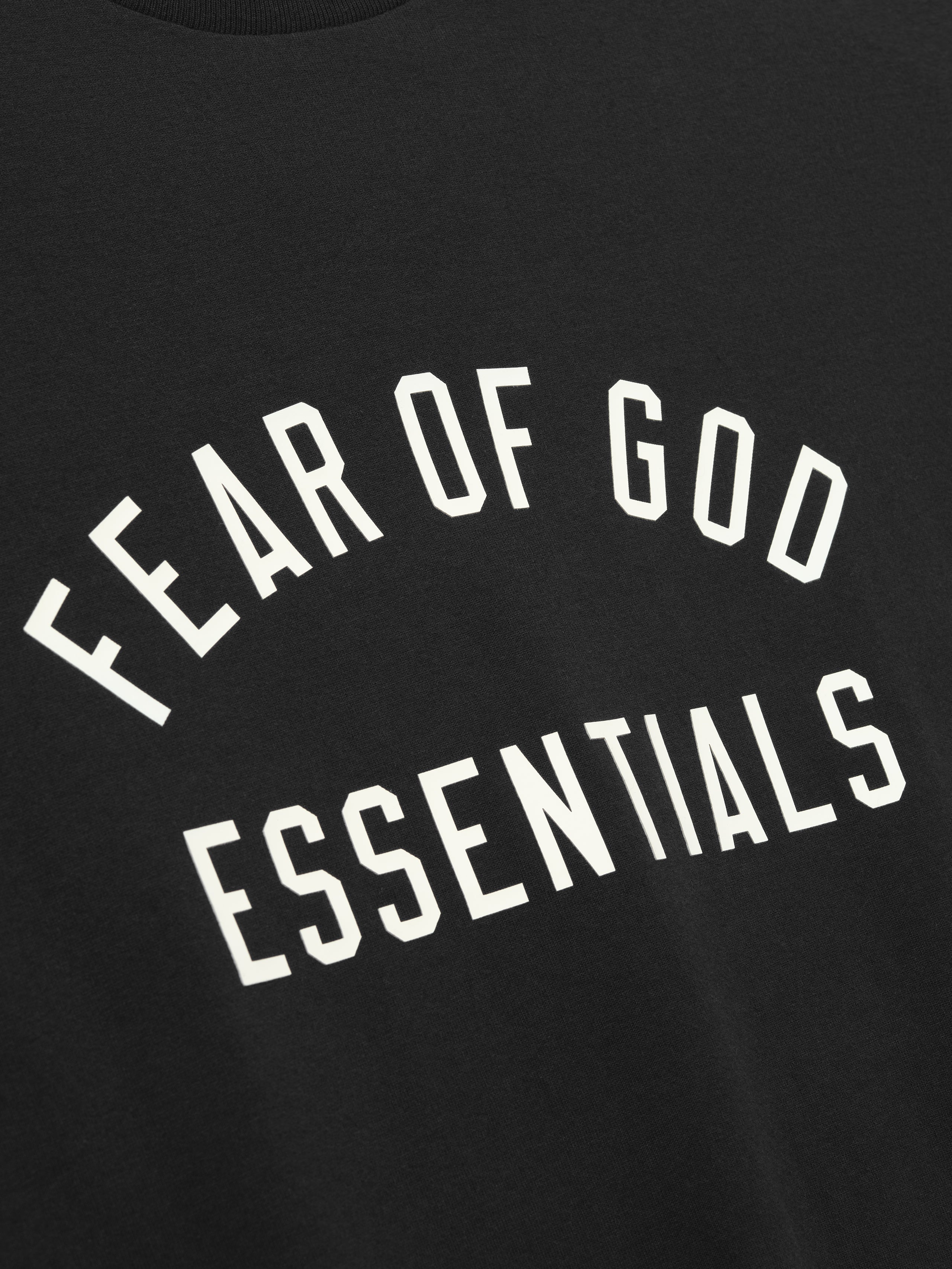 Close-up of black fabric with white "FEAR OF GOD ESSENTIALS" text printed in arched design on front panel