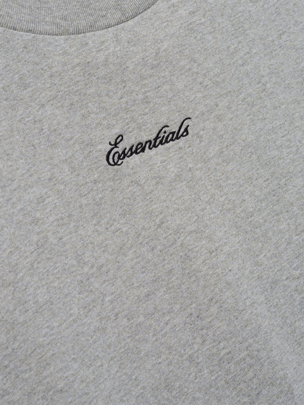 Close-up of the Kids Signature 90s Tee in soft concrete heather fabric featuring black cursive Essentials embroidery on the chest for a casual, classic look.