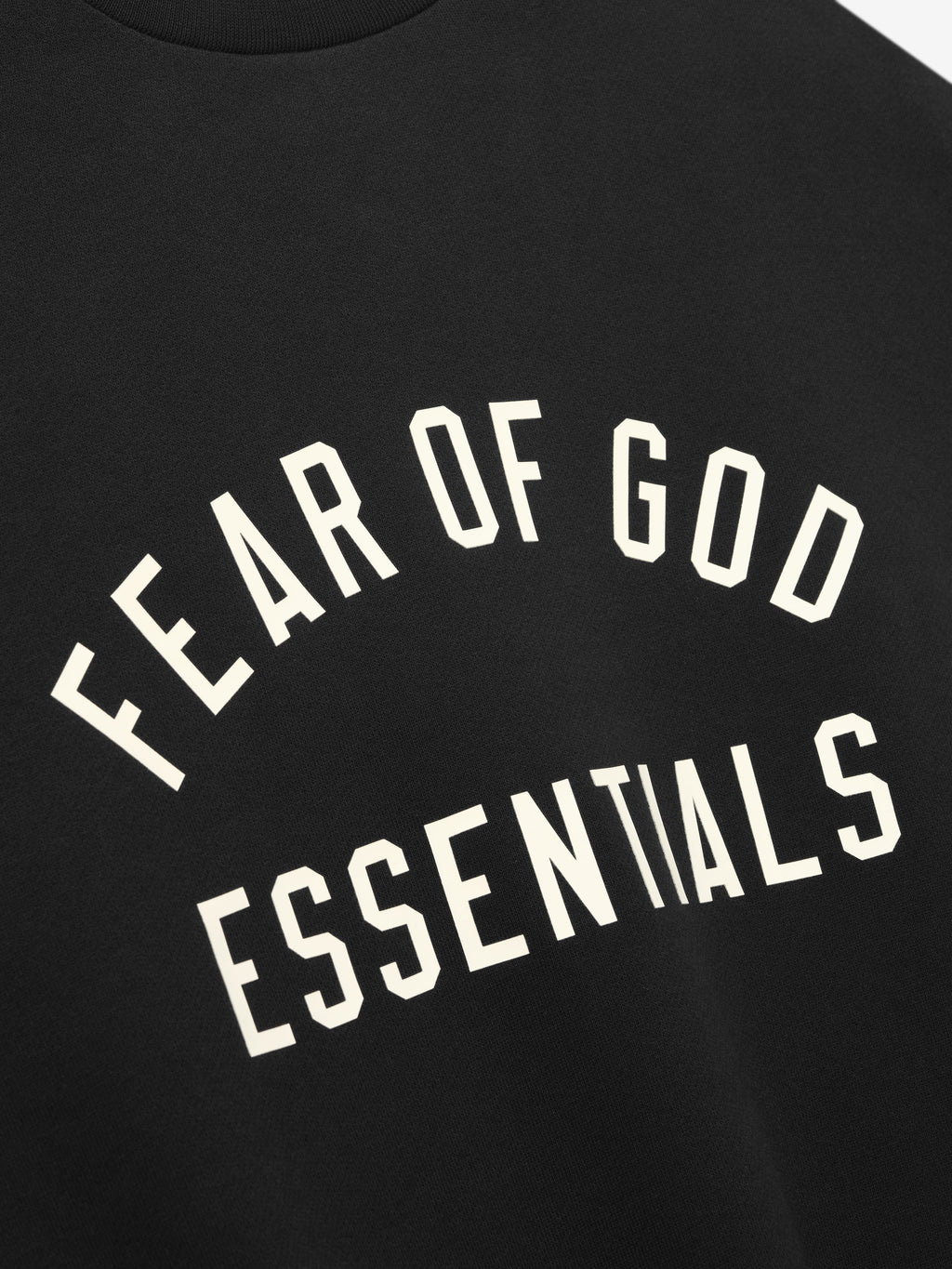 Close-up of black fabric with bold white "FEAR OF GOD ESSENTIALS" text in an arch design on front center
