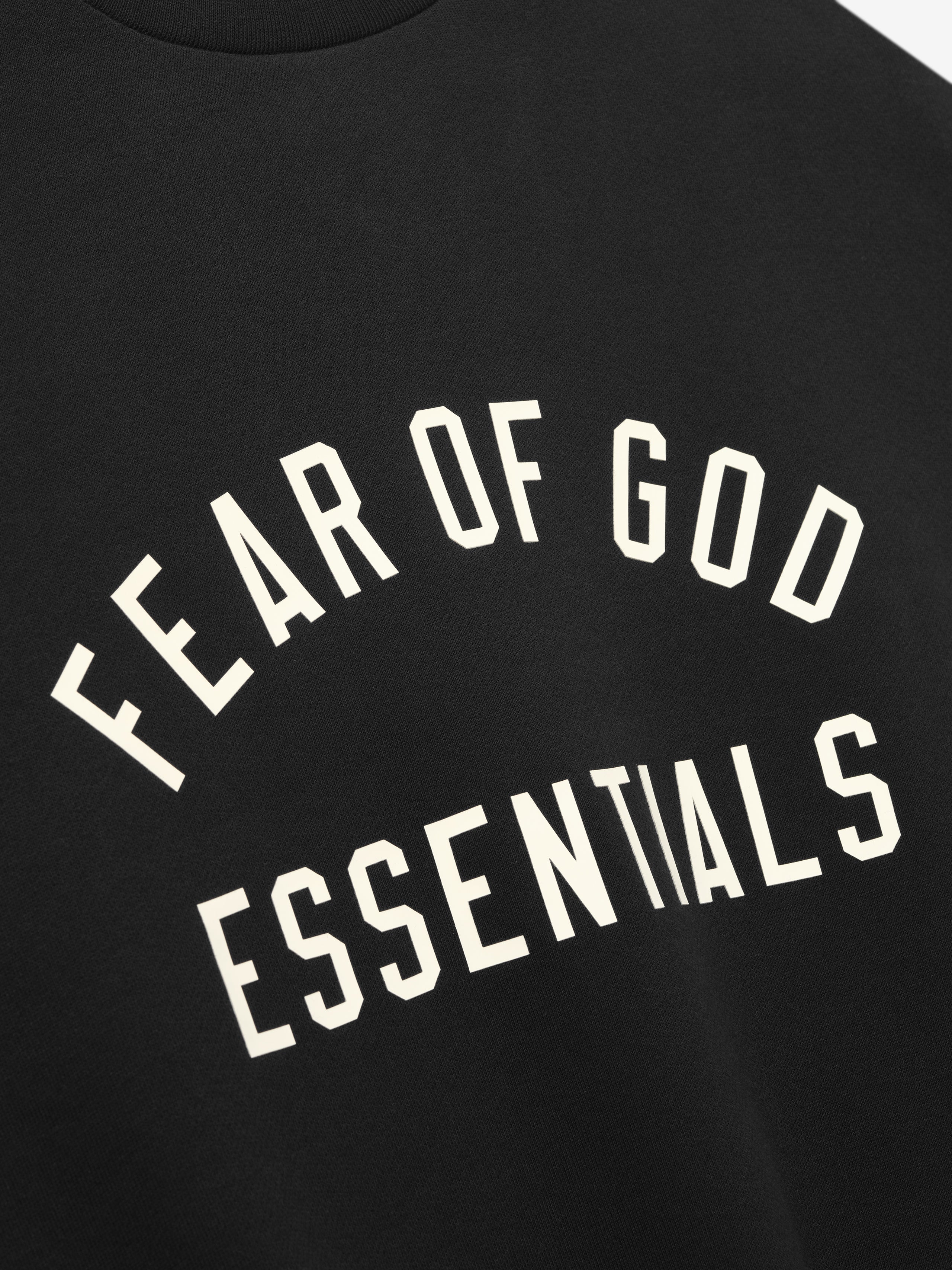 Close-up of black fabric with bold white "FEAR OF GOD ESSENTIALS" text in an arch design on front center
