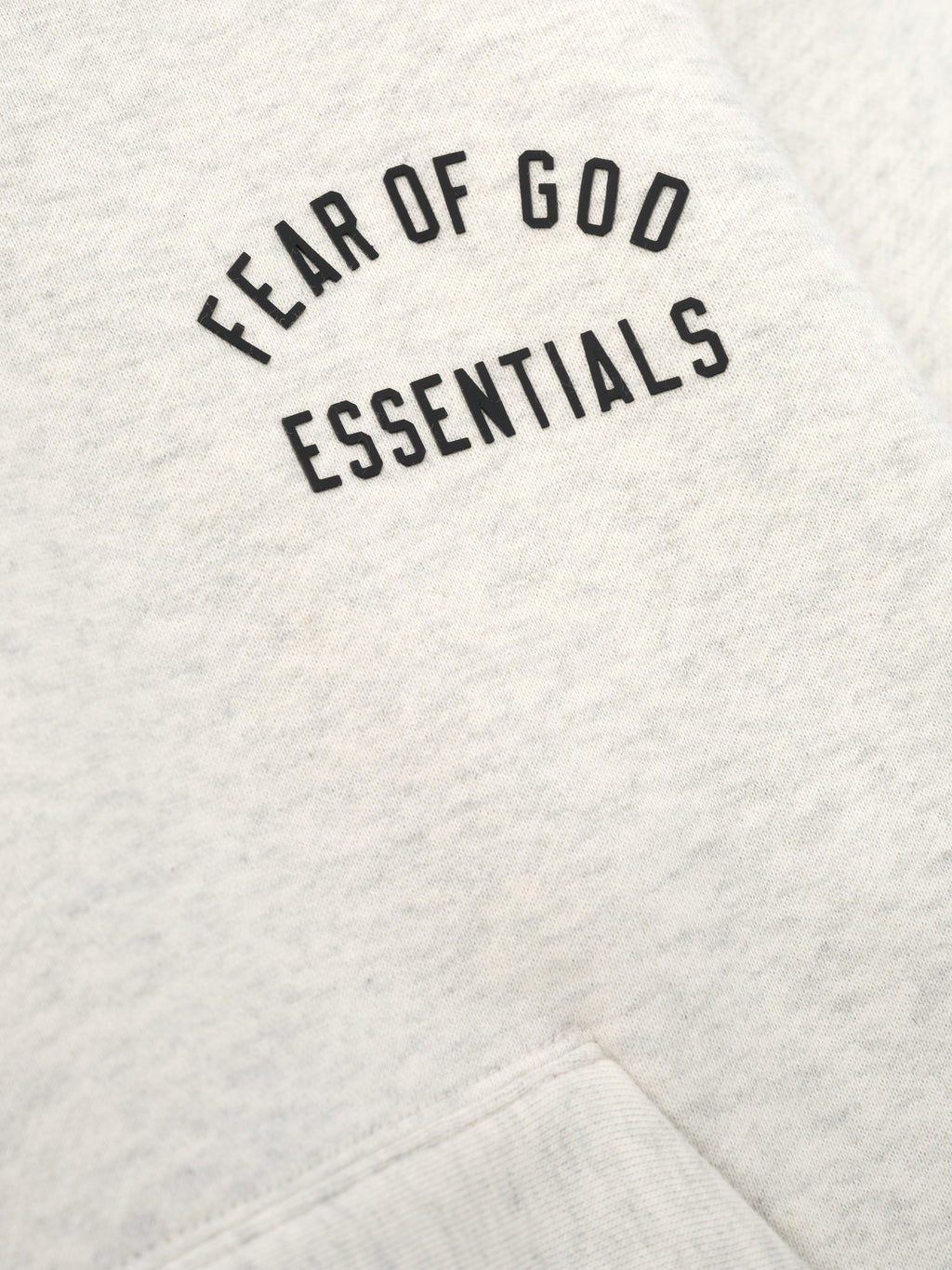 close-up of light beige kids hoodie fabric with Fear of God Essentials logo printed on chest in black text