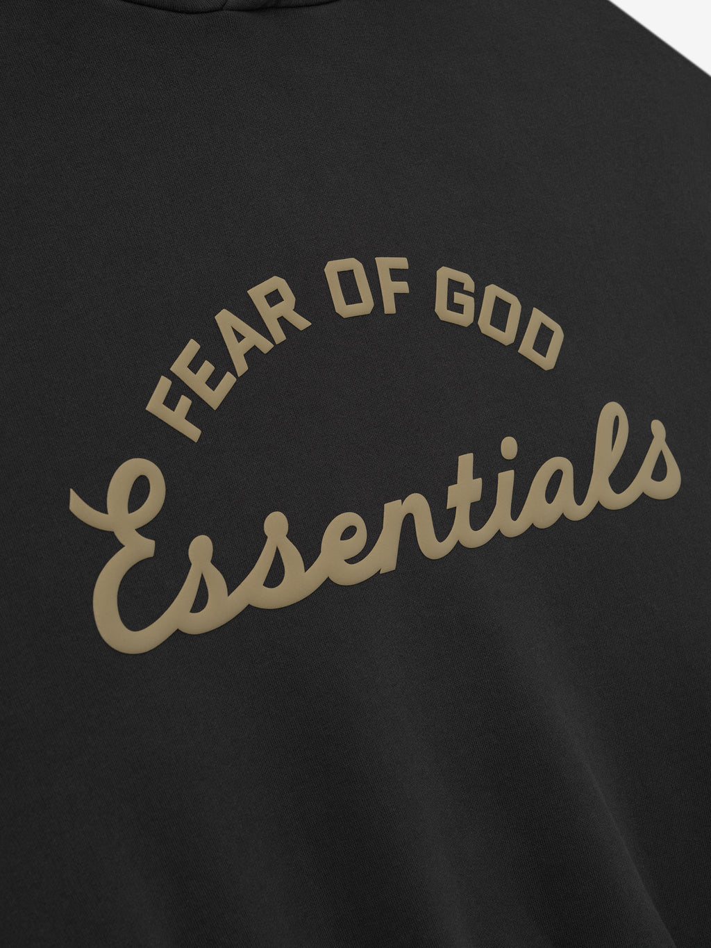 close-up of black kids hoodie with curved Fear of God Essentials training logo printed in tan puff ink on front
