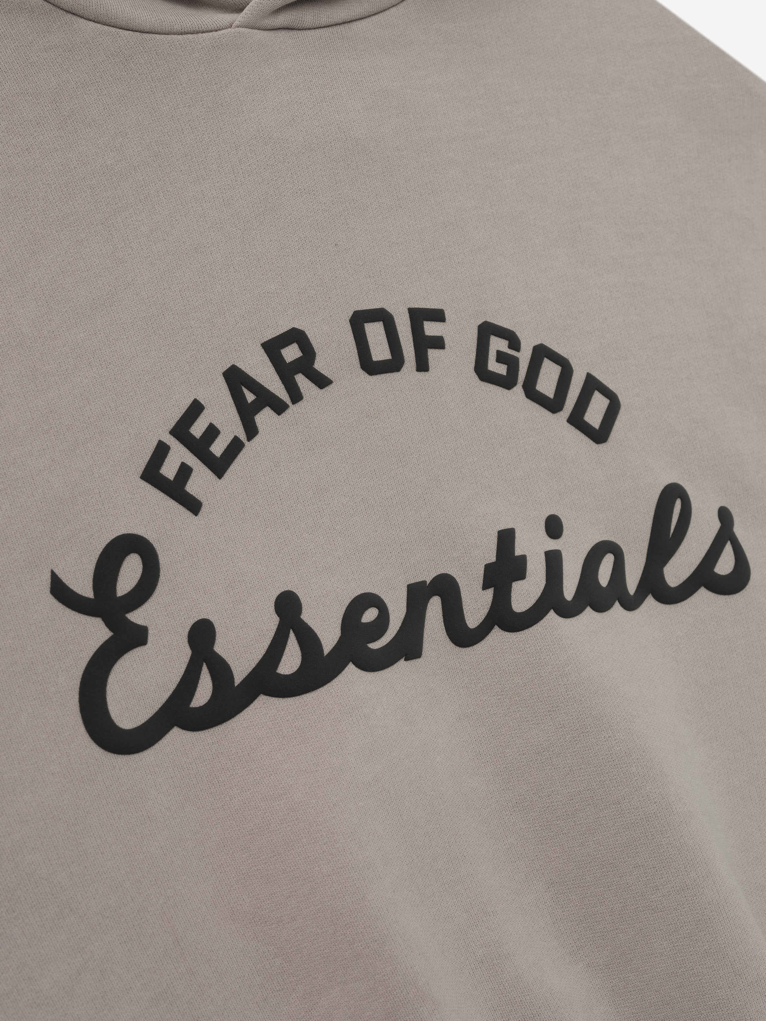 close-up of muted taupe kids hoodie with curved Fear of God Essentials logo printed in black on front