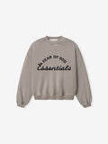 Light brown crewneck sweatshirt with black "Fear of God Essentials" text in curved and script fonts on front center