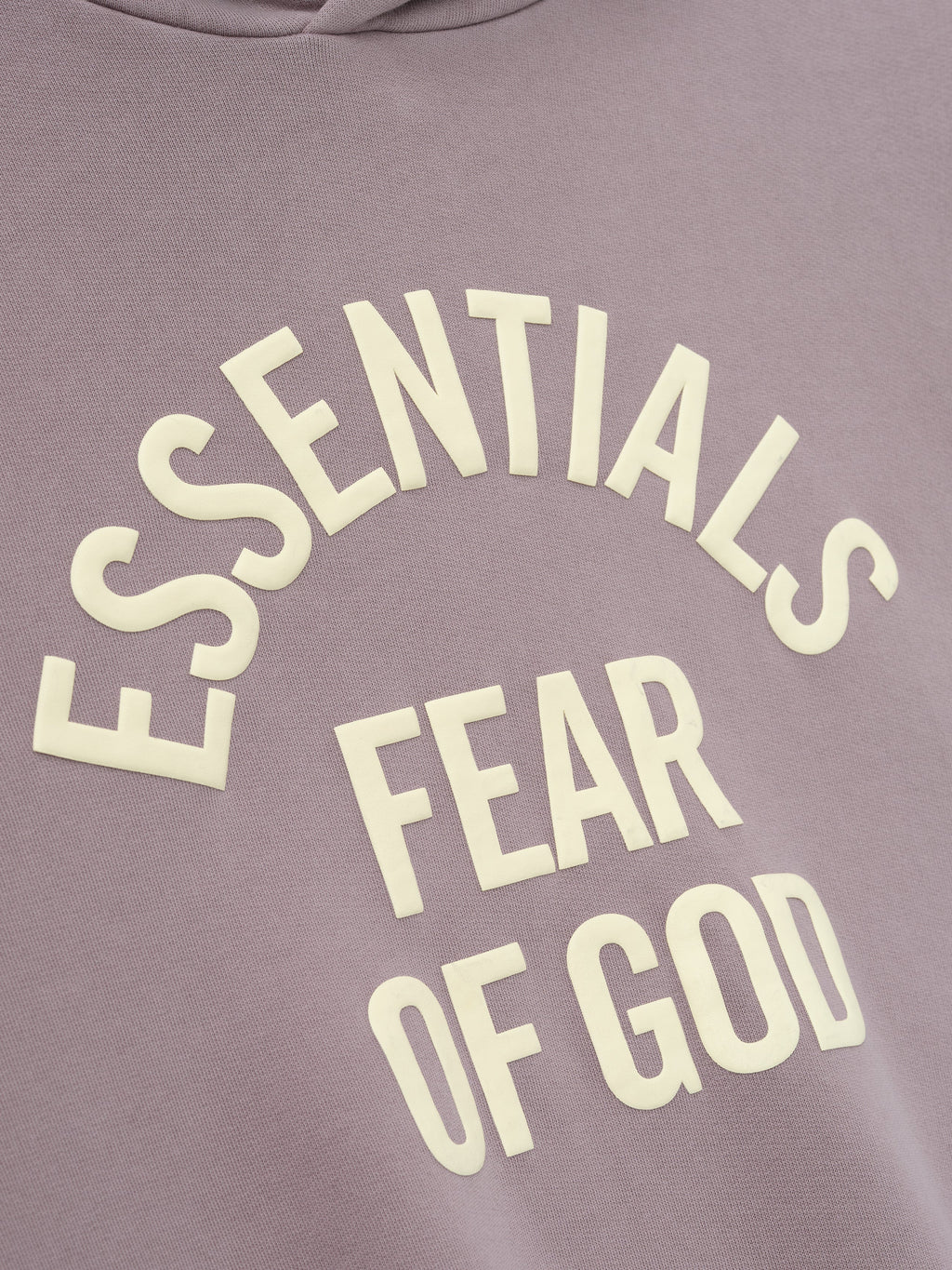 close-up of muted mauve pigment-dyed fleece fabric with raised cream Essentials Fear of God text printed in curved layout